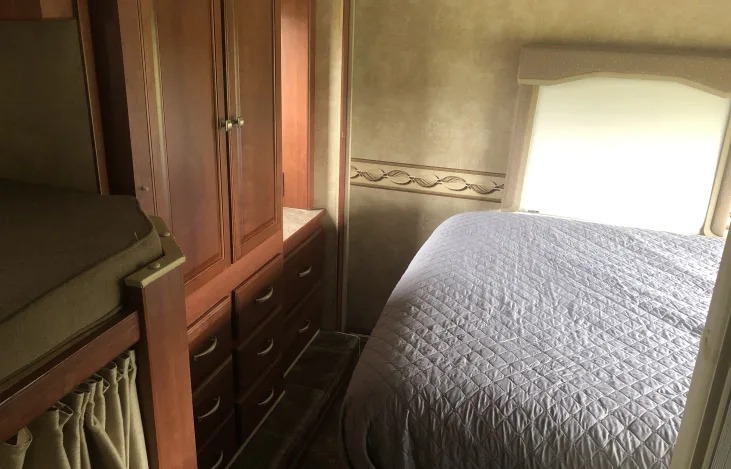 Interior view of an RV rental showing a main bed, bunk beds, and wood cabinetry with storage. Ideal for family trips.. Winnebago Chalet 2014