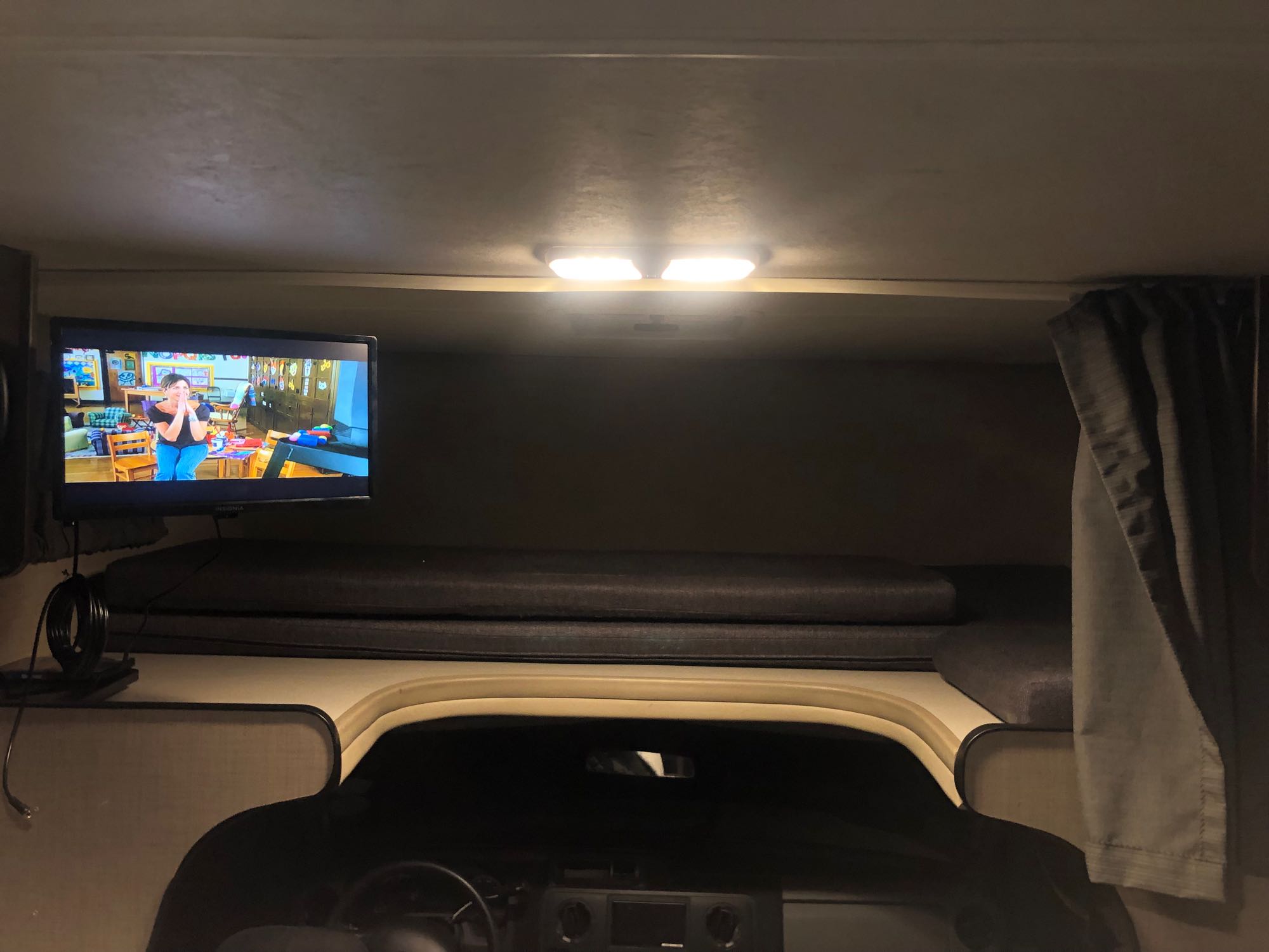 Cozy RV rental interior showing a TV, overhead bunk with cushions, and the front cabin area, well-lit by ceiling lights.. Thor Majestic 2018