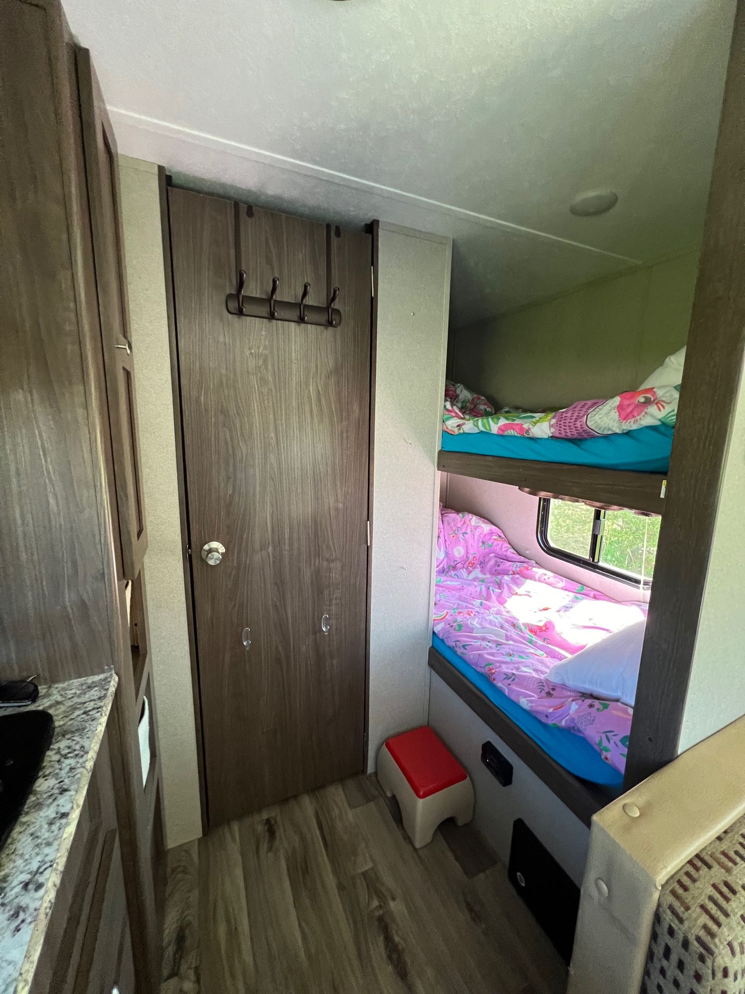 RV rental interior: cozy bunk beds with colorful bedding, a wood-grain door, and a glimpse of the kitchen counter.. Keystone RV Hideout LHS 2019