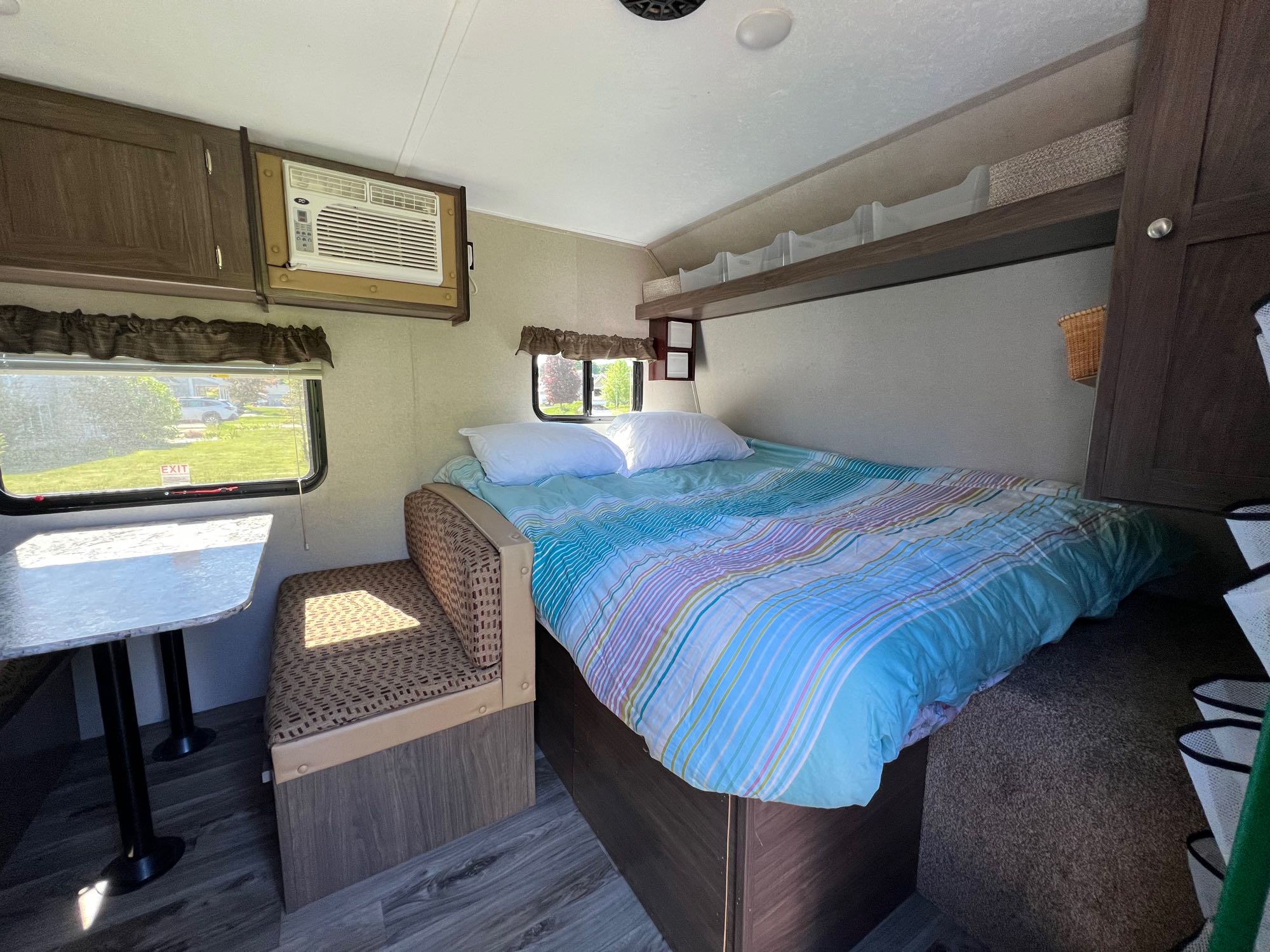 Cozy RV rental interior featuring a bedroom with a striped comforter, dinette, and wall-mounted AC unit.. Keystone RV Hideout LHS 2019