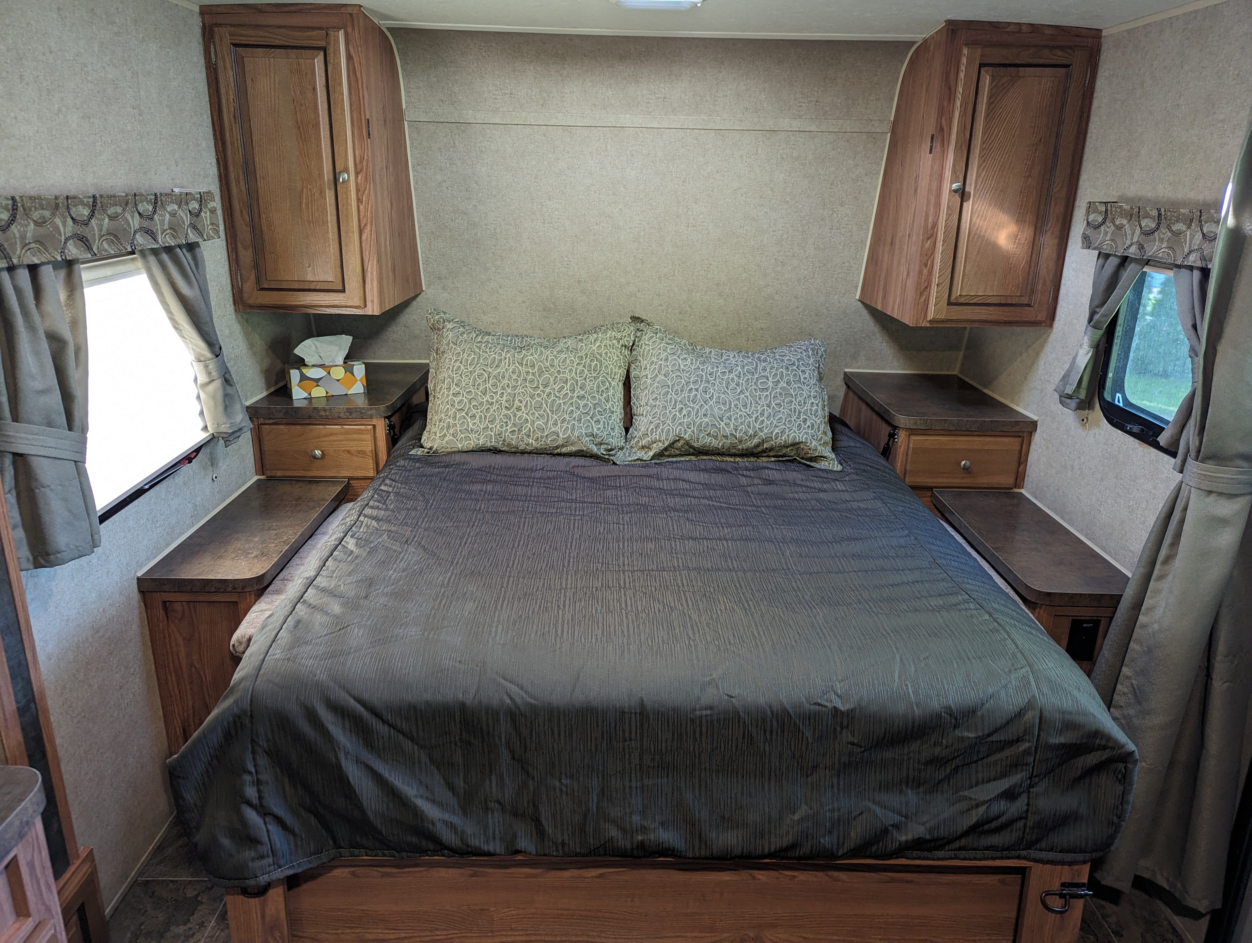 Cozy RV rental bedroom featuring a queen bed, two patterned pillows, wooden cabinets, and windows with curtains.. Forest River Rockwood Mini Lite 2015