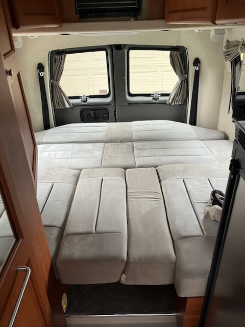 Cozy rv rental interior: Rear view of a camper van bed with gray cushions and windows with curtains.. Roadtrek Roadtrek Class B 2010