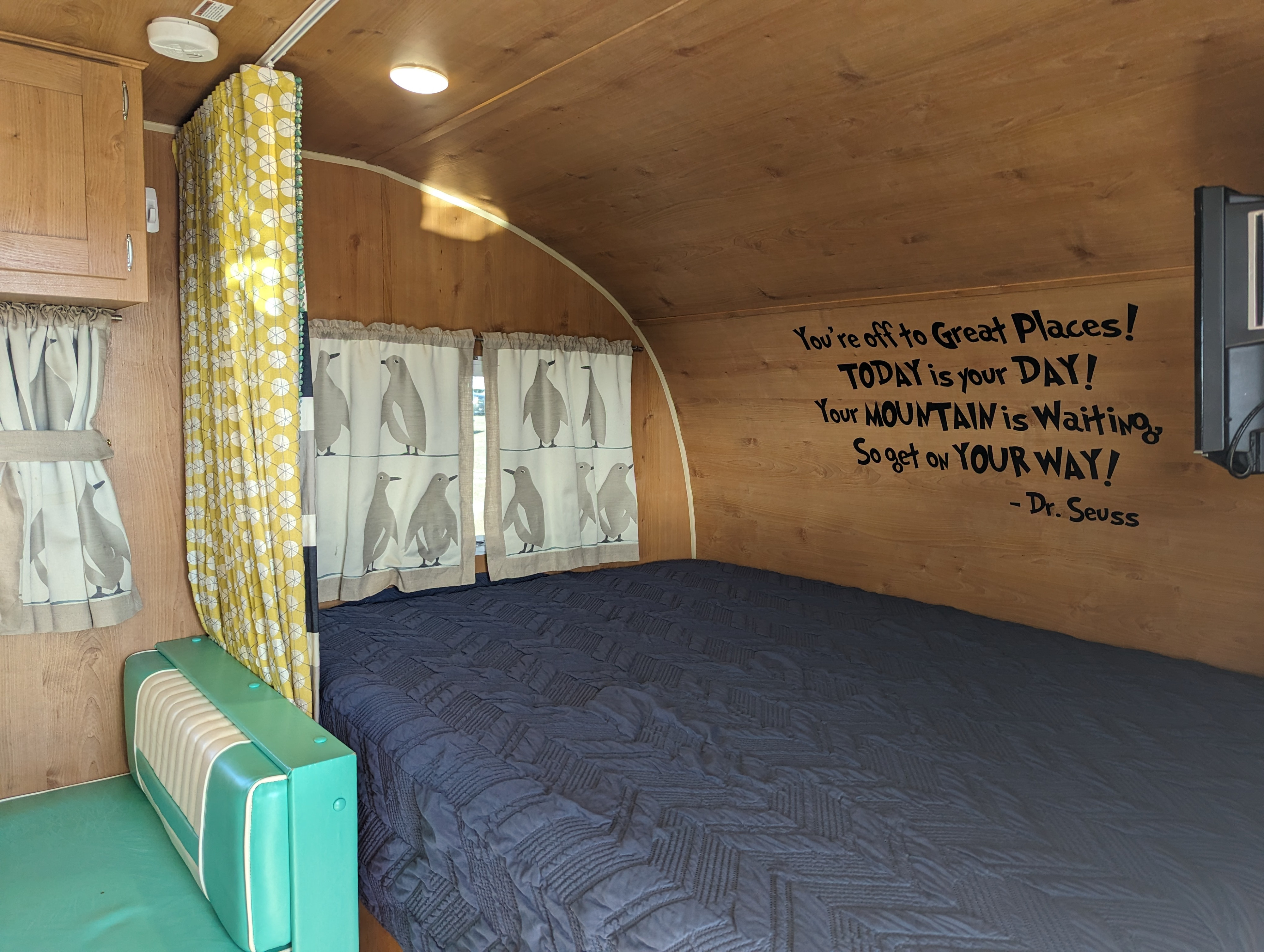RV rental interior: cozy bedroom with wooden panels, blue bed, unique penguin curtains, and Dr. Seuss quote.. Riverside Rv Retro 2020