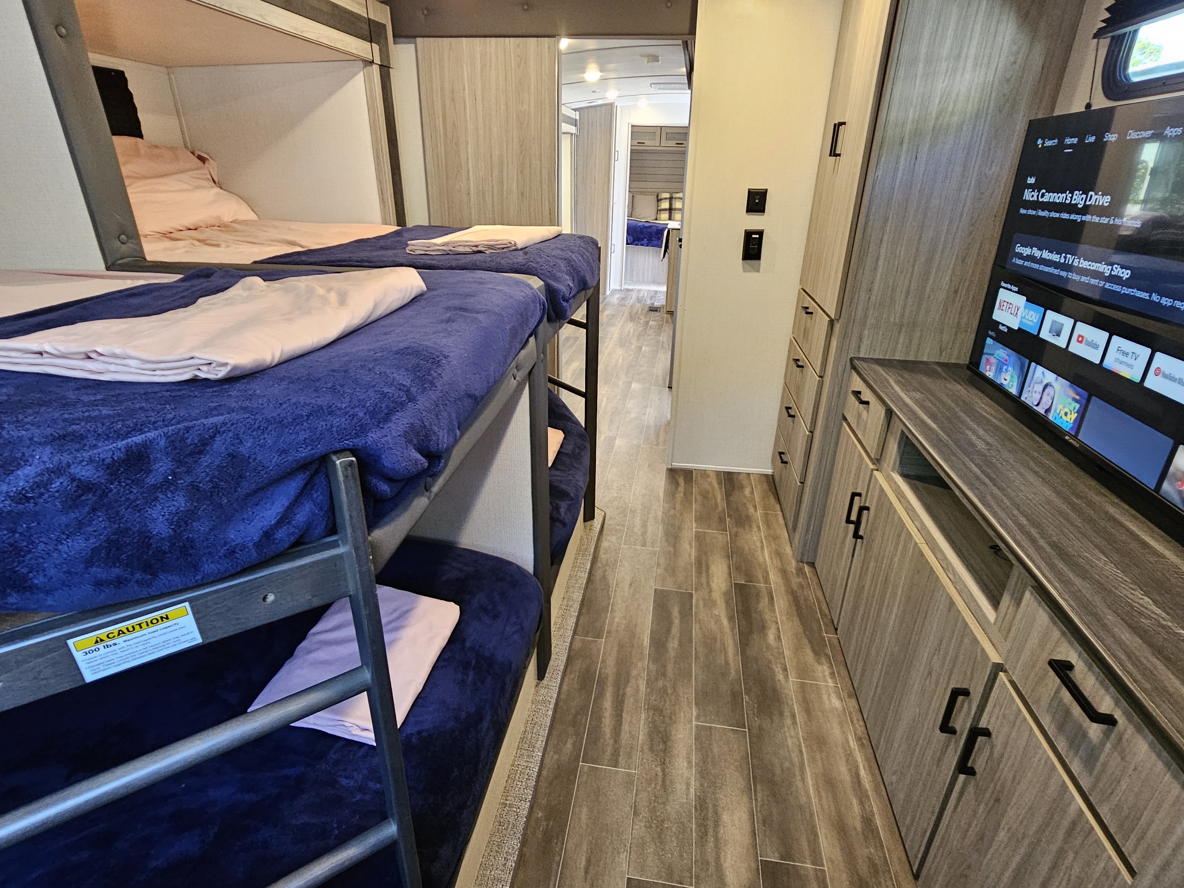 Modern RV rental interior features cozy bunk beds, a smart TV for entertainment, and sleek wood-look flooring.. Keystone Passport 2022