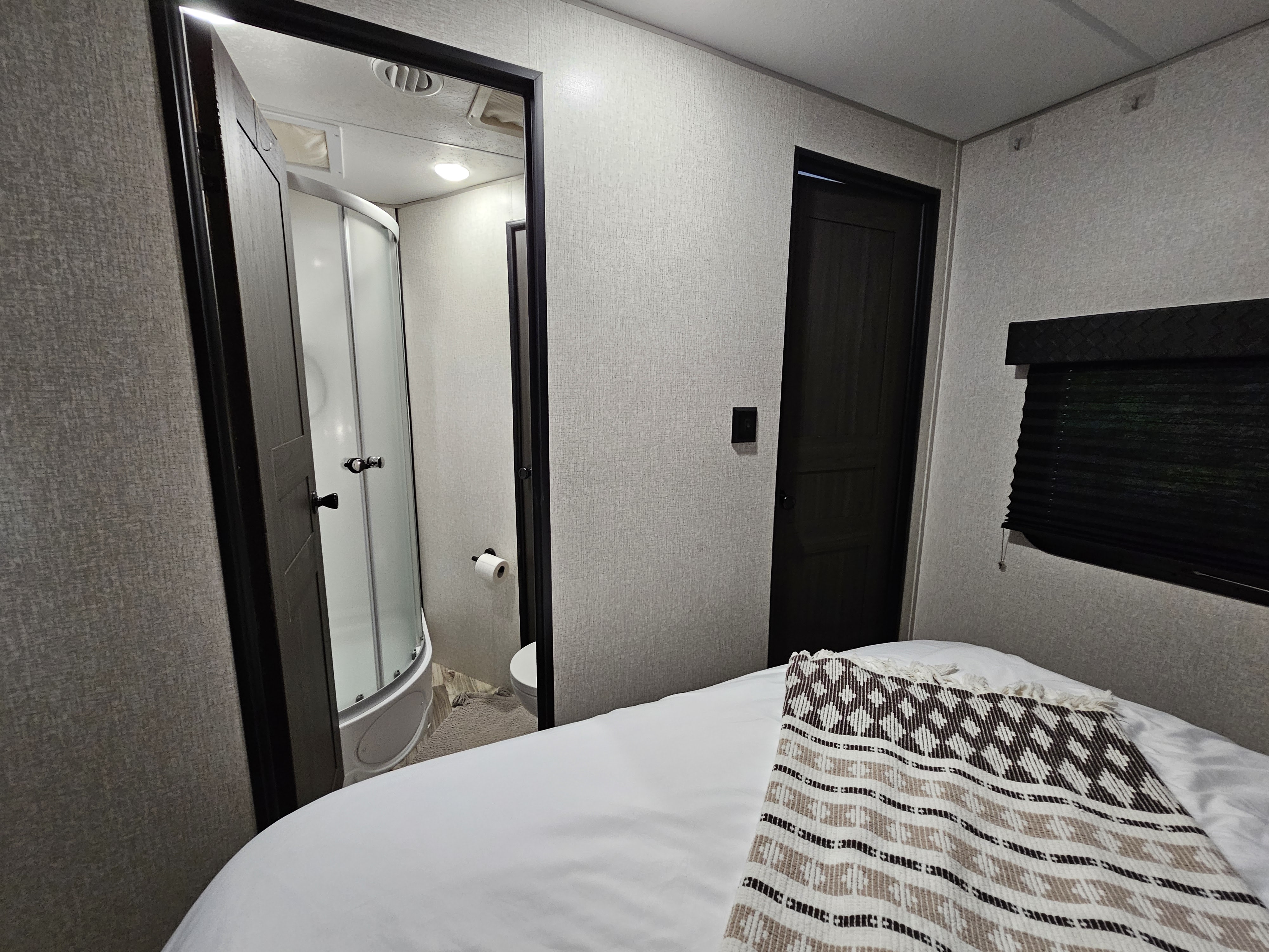 Inside an RV rental: bedroom with a cozy bed and blanket, offering a view into the compact bathroom with a curved shower.. Venture Rv Sporttrek 2022