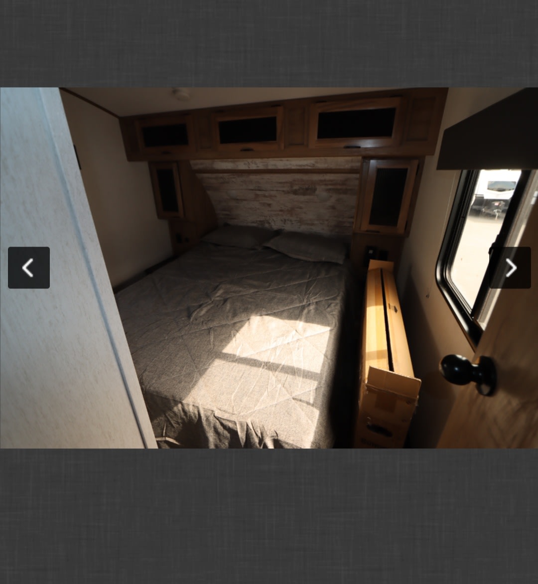 Inside an RV rental: a cozy bedroom with a bed, rustic headboard, overhead cabinets, and a window letting in sunlight.. Forest River Other 2024