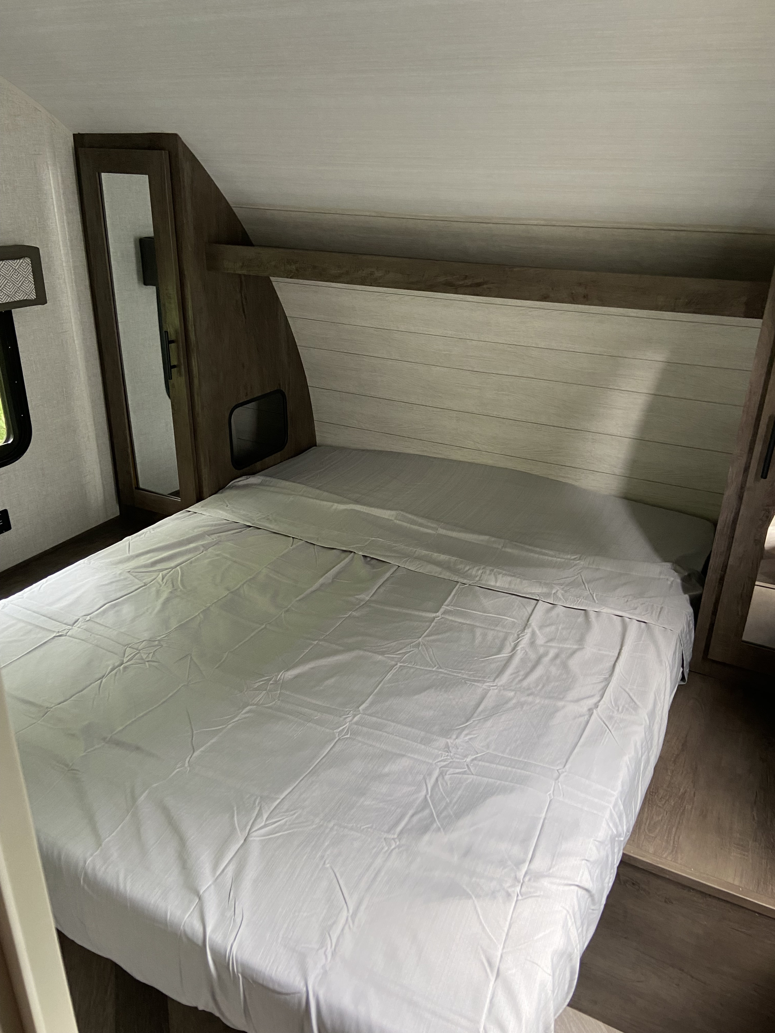 This clean and cozy RV rental bedroom features a bed with light sheets, a wood headboard, and mirrored cabinets.. Forest River Salem Cruise Lite 2021