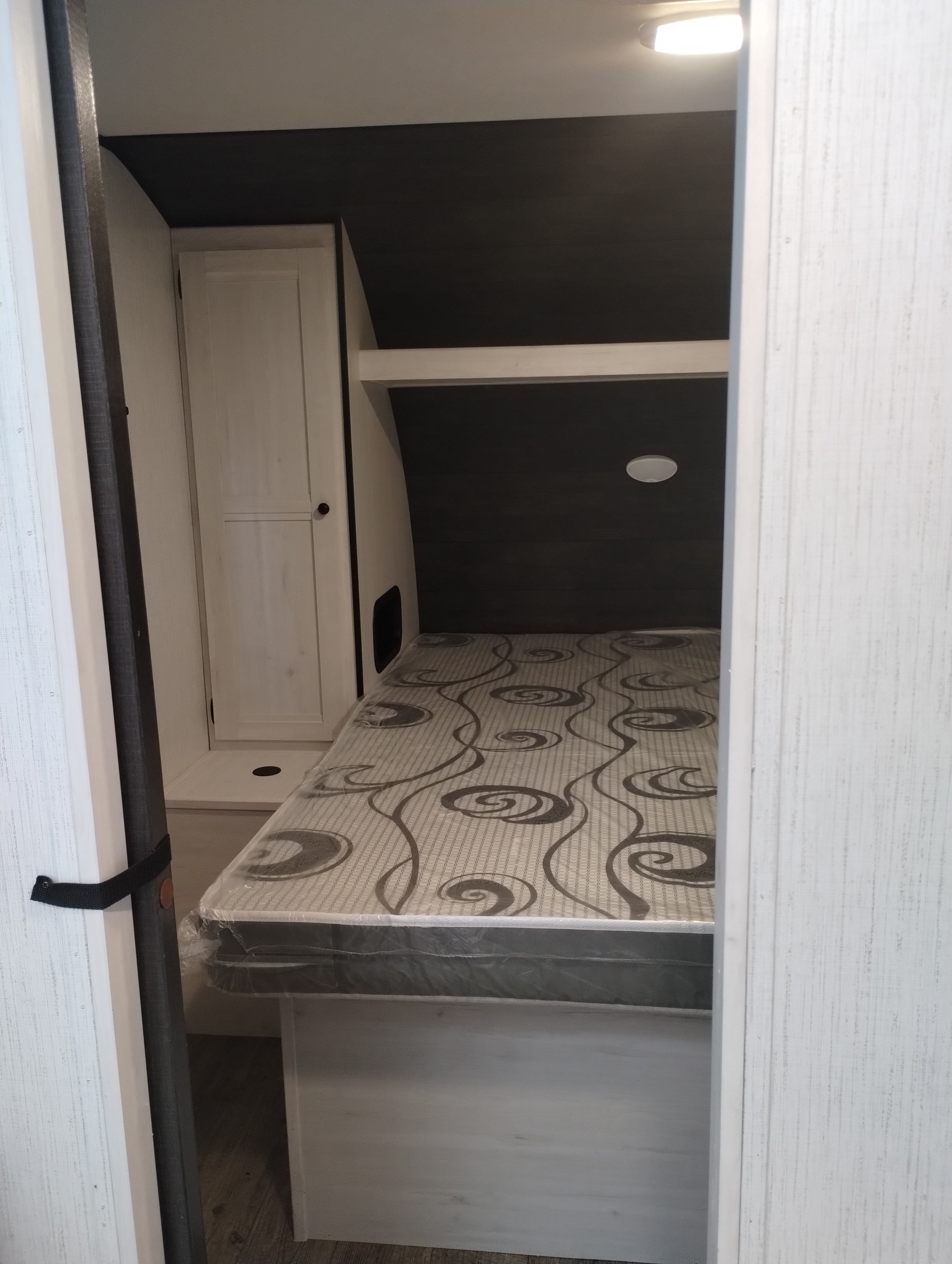 Compact RV rental bedroom with a bed featuring a patterned mattress, cabinet, and overhead light. Ideal for travel.. Heartland RVs Trail Runner 2022