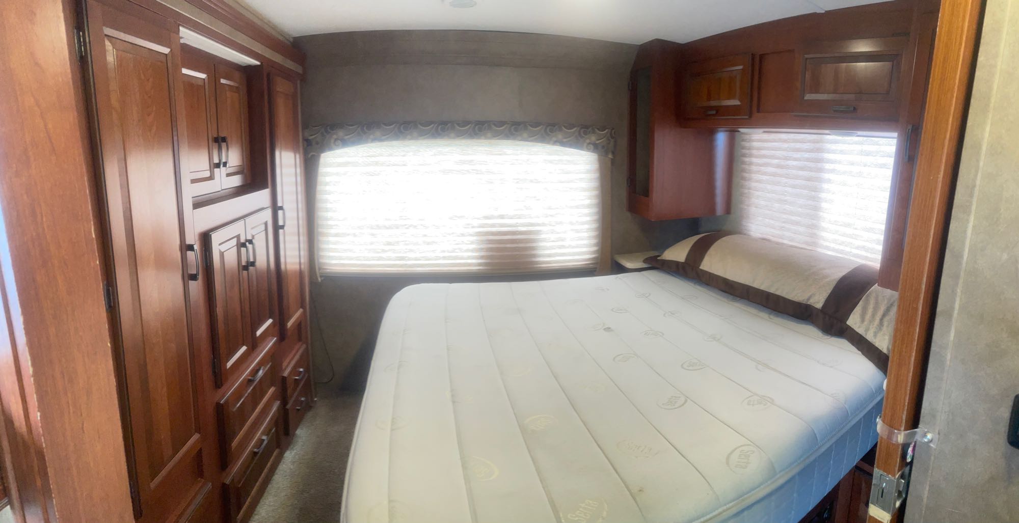 RV rental bedroom: a clean Serta mattress on the bed, extensive wooden cabinetry, and a bright window with blinds.. Forest River Sunseeker 2016