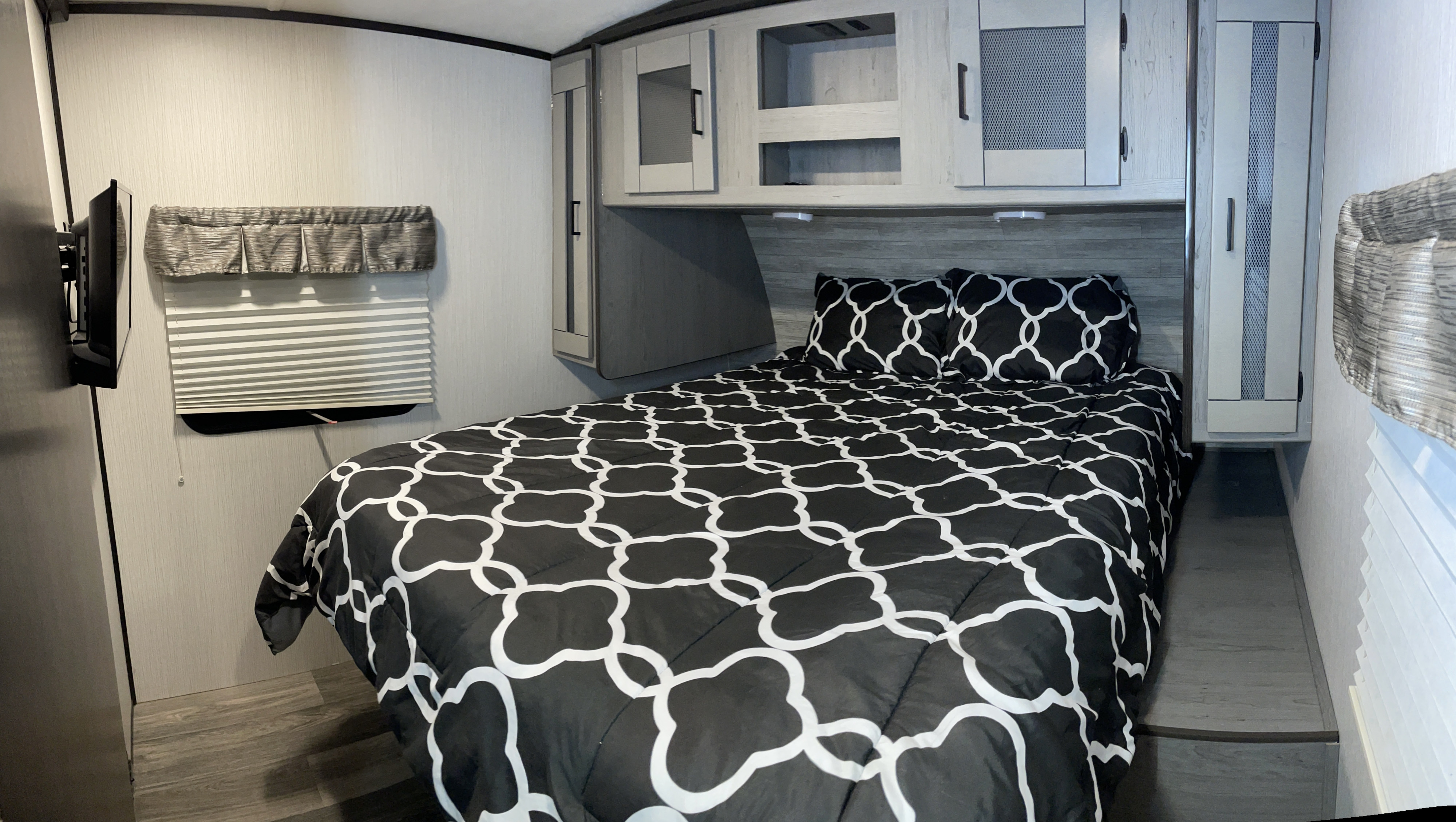RV rental bedroom with a black & white patterned bed, overhead cabinets, wall-mounted TV, & side storage.. Heartland RVs Mallard 2021