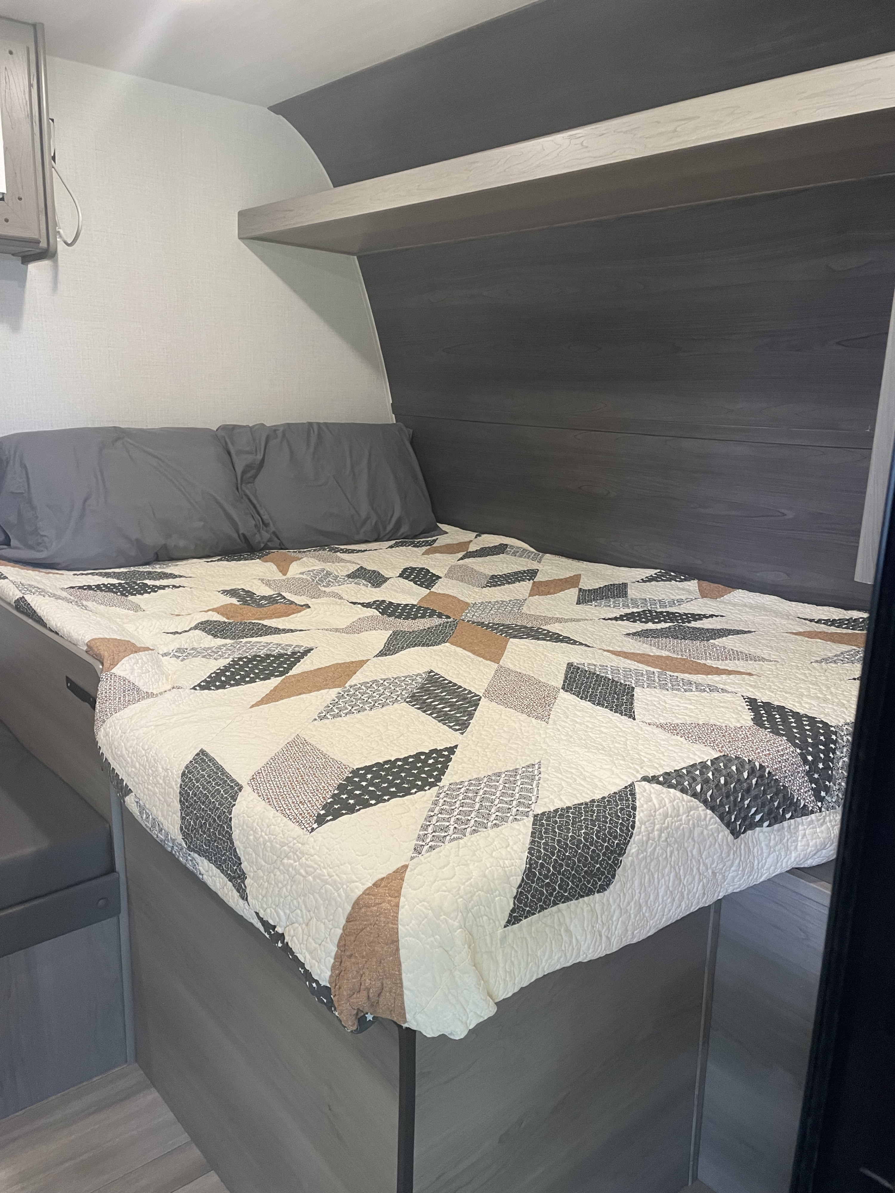Cozy RV rental bedroom with a modern geometric quilt in cream, brown & gray, dark gray pillows, and sleek wood paneling.. Keystone RV Hideout Sport 2024