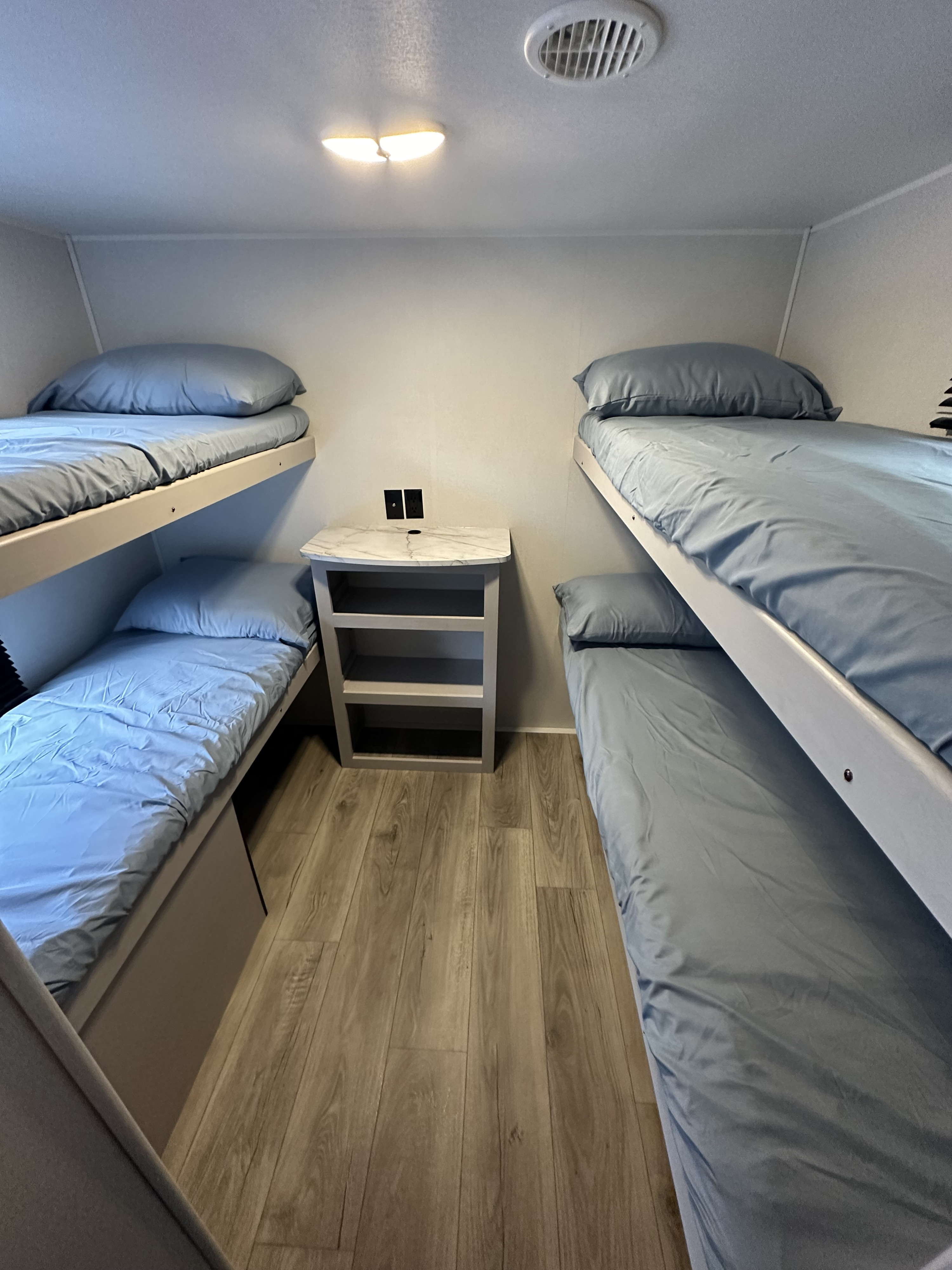 Inside an RV rental, this bunk room has two sets of bunk beds with blue bedding, a central nightstand, and light wood floors.. Heartland RVs Prowler Lynx 2024