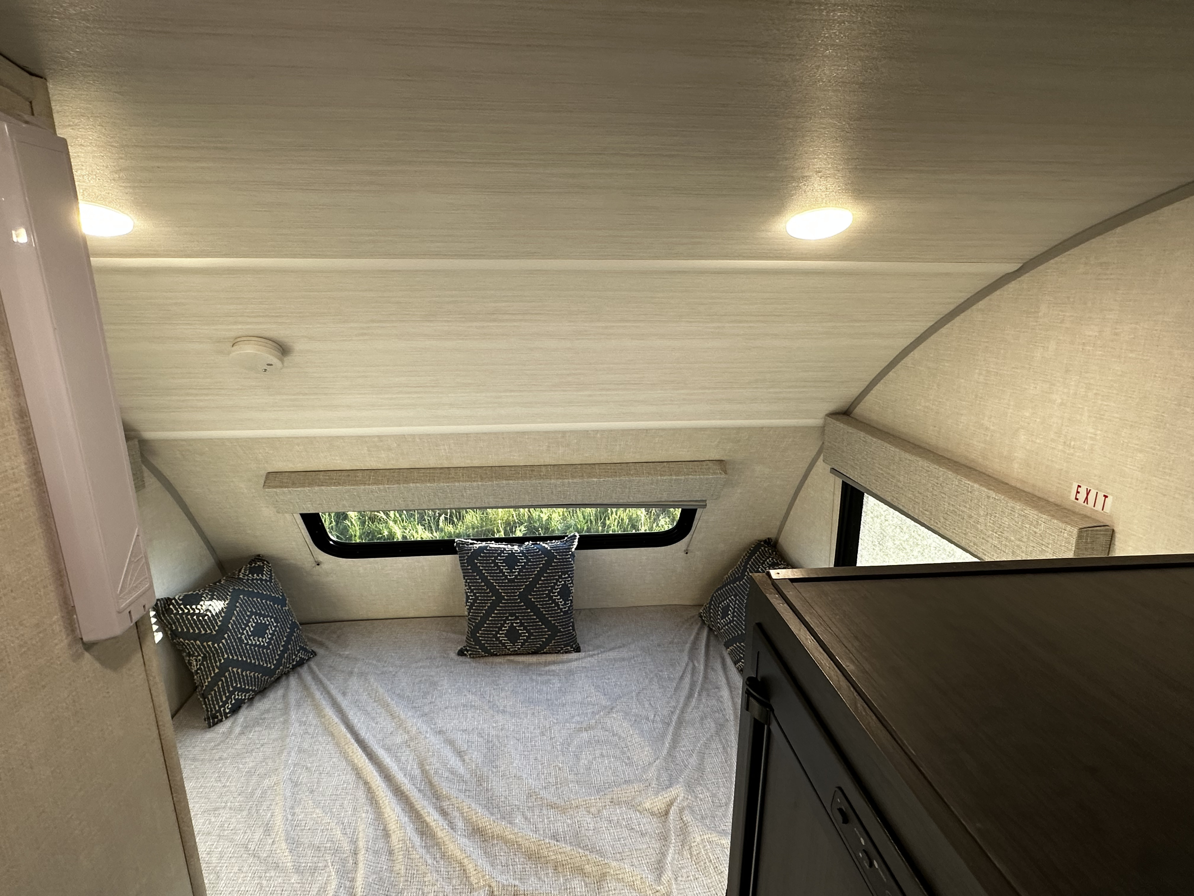 An RV rental's cozy sleeping area, featuring a bed, patterned pillows, window view, and overhead lights.. Forest River RPOD171C 2024