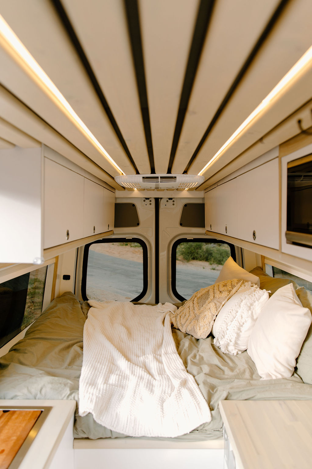 Inside a modern RV rental van: a cozy bed with pillows, sleek overhead cabinets, and ambient ceiling lights illuminating the space.. Mercedes Sprinter 2021