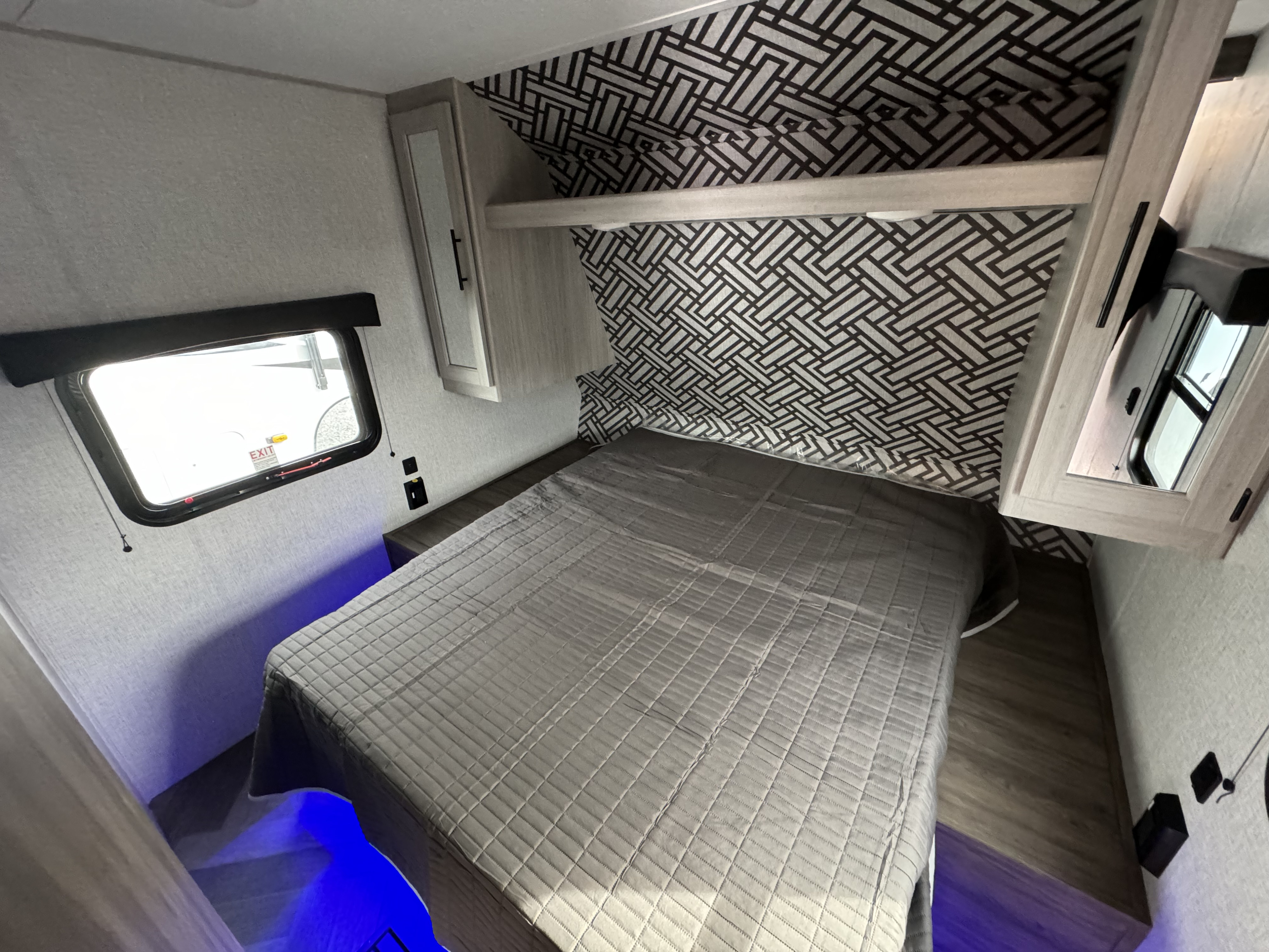 Spacious RV rental bedroom with gray bed, patterned wall, overhead storage, and blue accent lighting.. Crossroads RV Zinger 2023