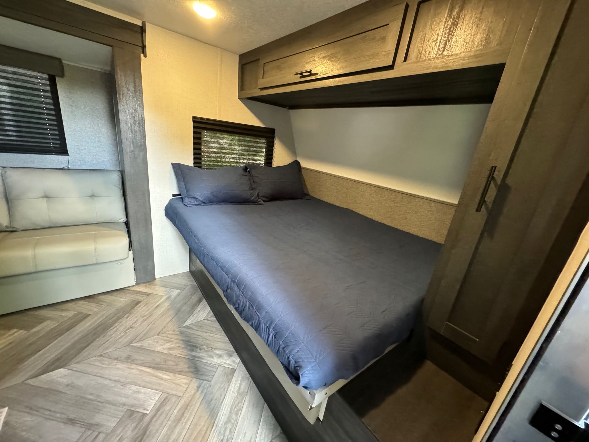 This RV rental offers a well-appointed bedroom with a bed, overhead cabinets, and a living area with a sofa.. Forest River 1680BSK 2021
