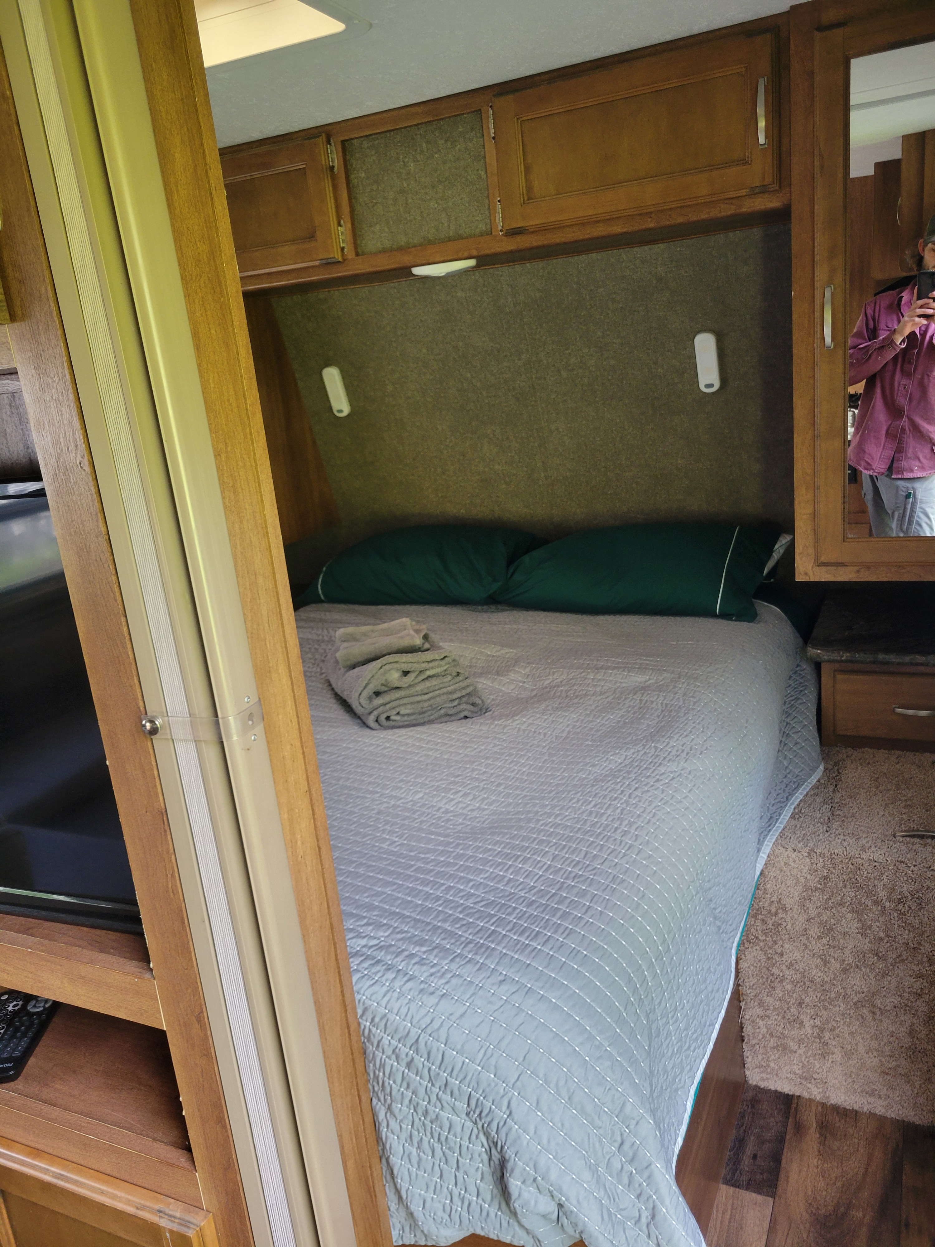 Inside a clean RV rental bedroom: bed with green pillows, folded towels, mirrored cabinet, and TV area.. Keystone RV Springdale 2018