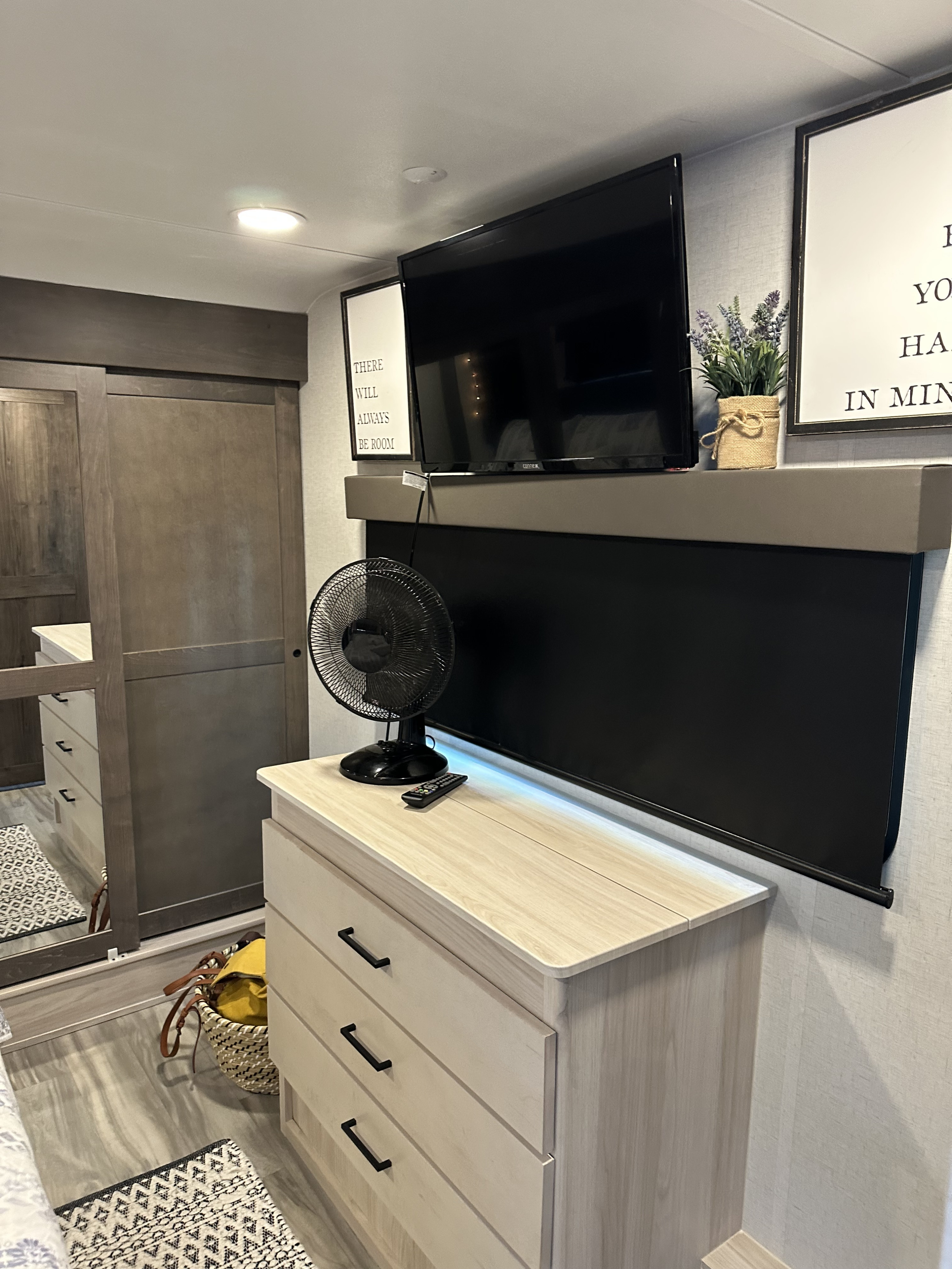 Cozy RV rental bedroom featuring a TV, dresser, fan, and barn-style sliding doors, providing modern living space.. Alliance RV Valor 2023