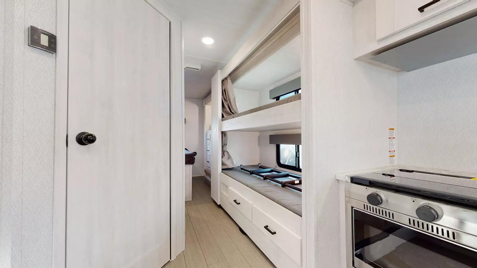 RV rental's functional interior: Hallway, stacked bunk beds, and a kitchen area with an oven/stove. Great for families.. EastWest Entrada 2024