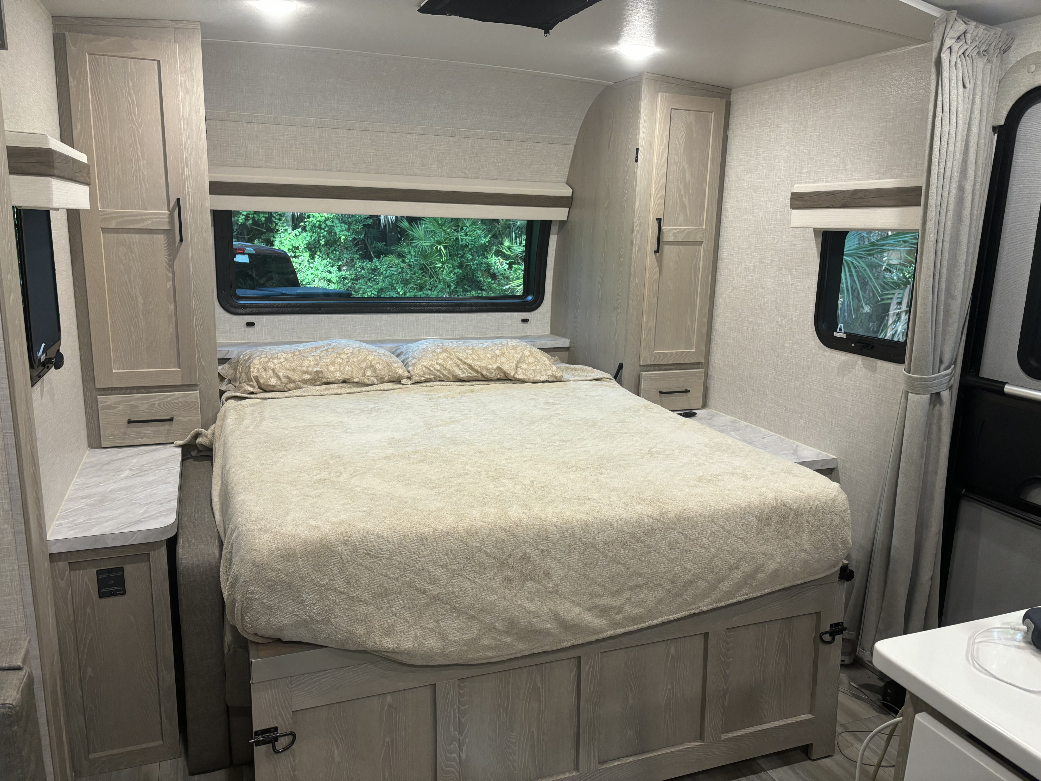 This RV rental's cozy bedroom features a light-colored bed, windows showcasing nature, and ample built-in storage.. Forest River Rockwood Mini Lite 2023