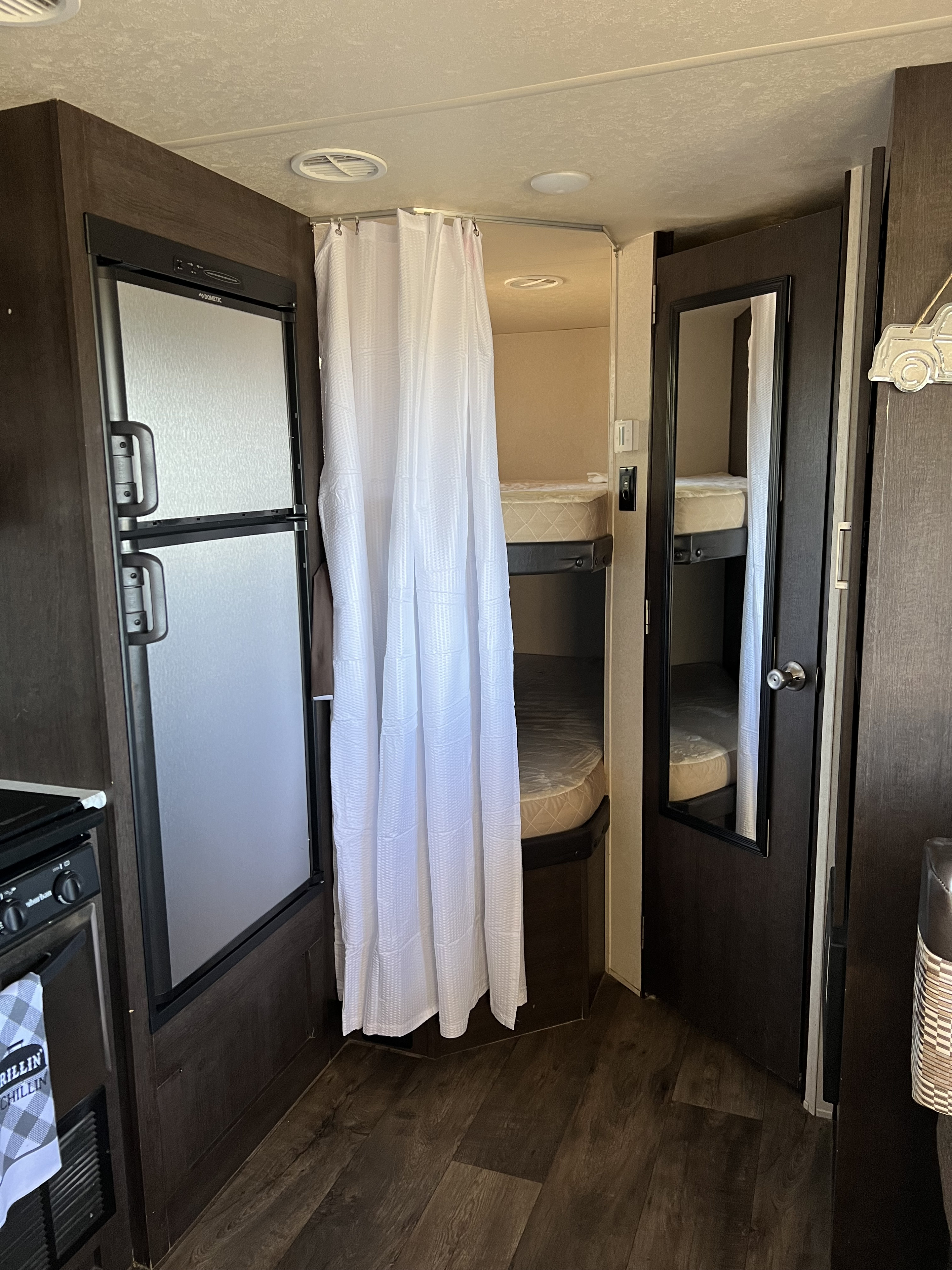 RV rental interior: kitchen with Dometic fridge & stove, plus private bunk beds with curtain & mirrored door.. Forest River Wildwood 2018