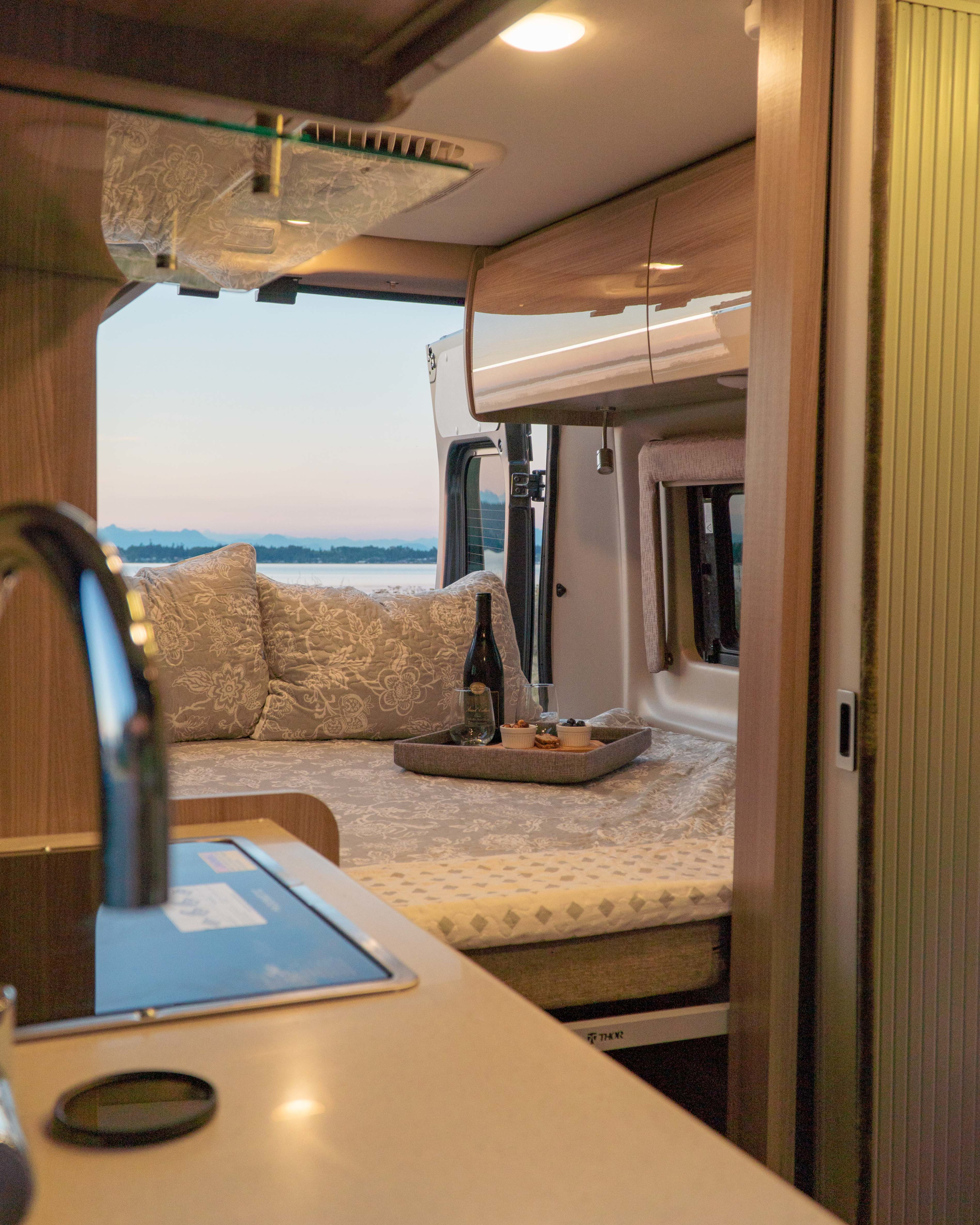 Cozy RV rental interior with a bed, wine, and snacks. Scenic water view out the back, perfect for travel.. Thor Motor Coach Tellaro 2023