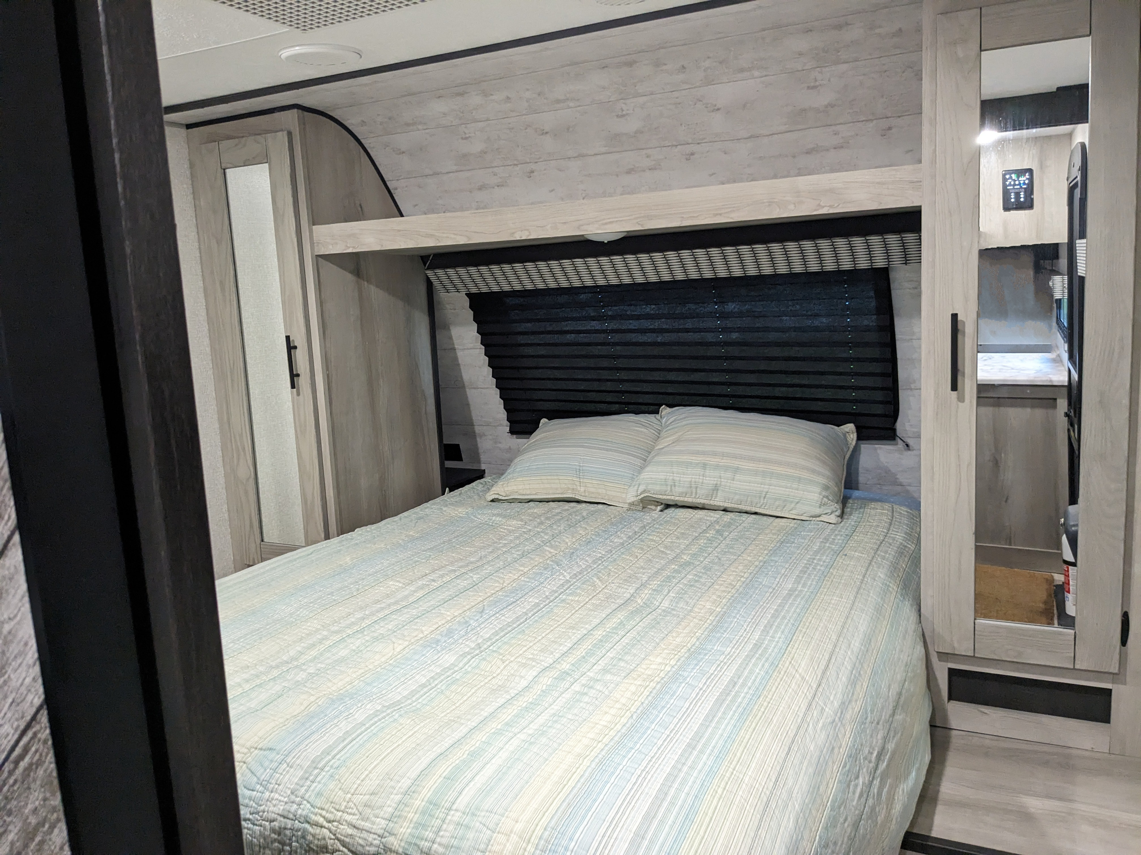 Cozy RV rental bedroom featuring a comfortable bed with striped bedding, overhead shelf, and built-in storage.. KZ C241bhkse 2022