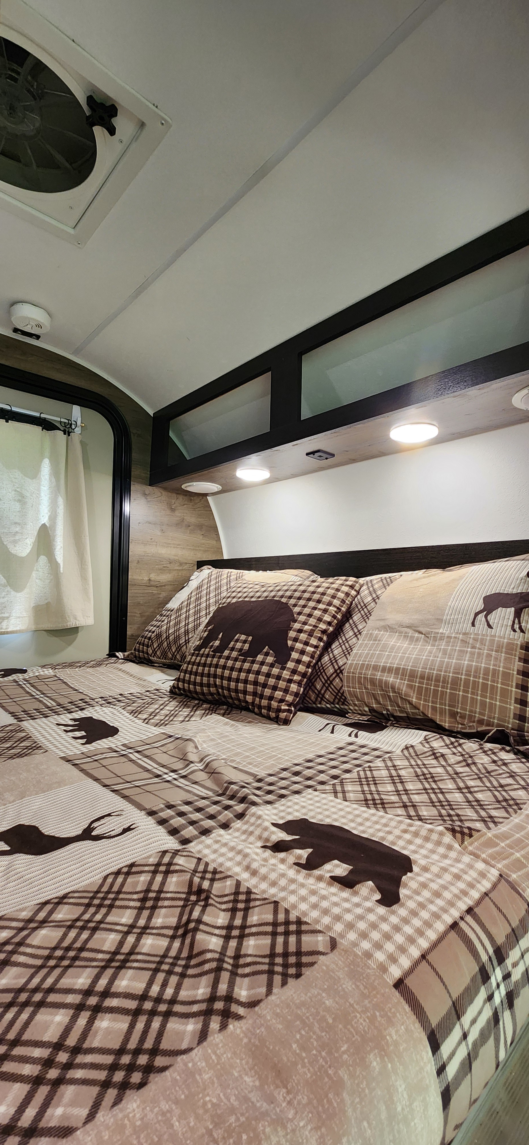 Comfortable RV rental bedroom featuring rustic plaid bedding with bear/deer designs, practical overhead storage, and reading lights.. Braxton Creek Free Solo 2022