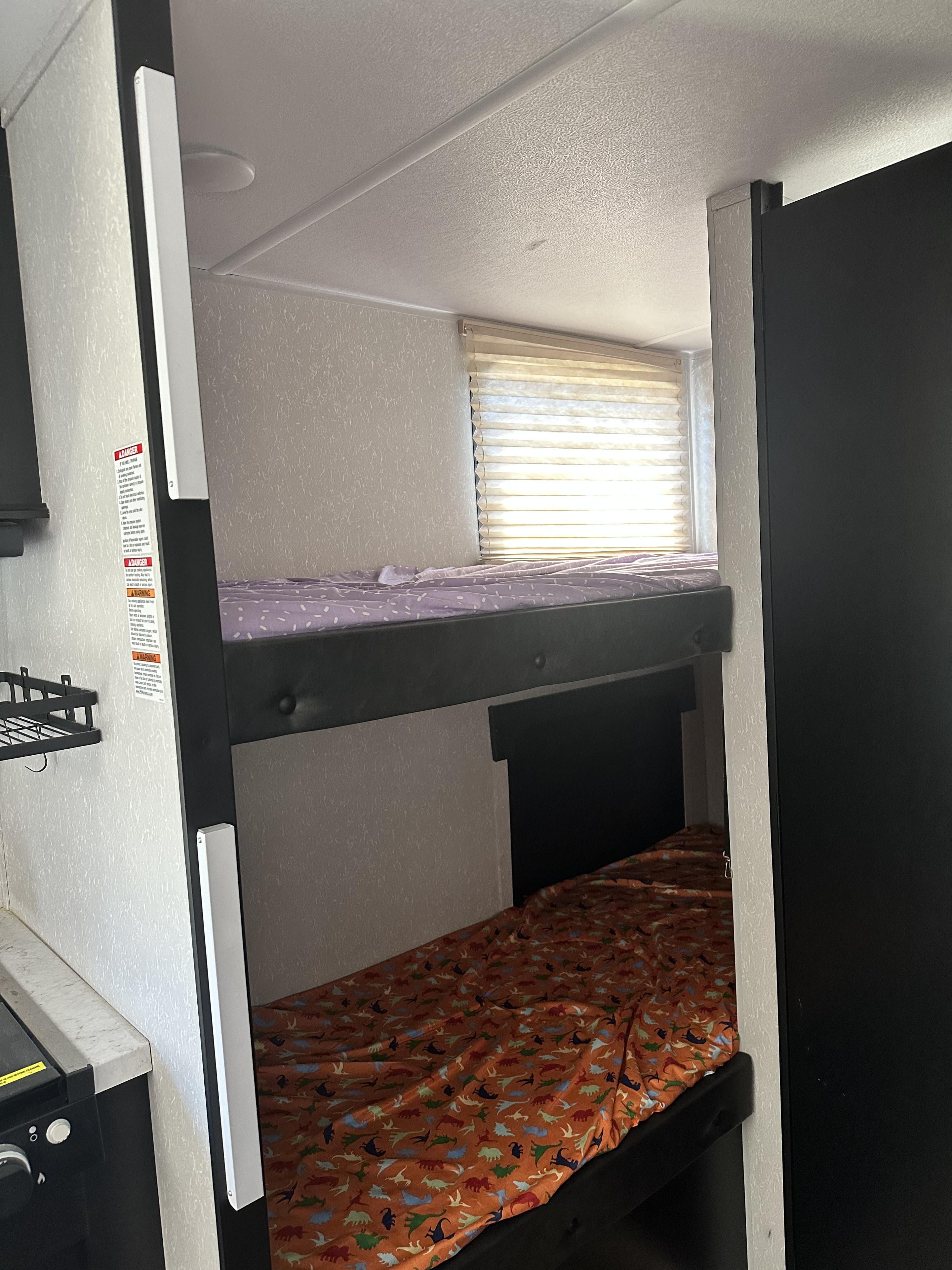 Inside an RV rental: cozy bunk beds with purple and dinosaur sheets, plus a window, perfect for family adventures.. Forest River Cherokee Wolf Pup 2021
