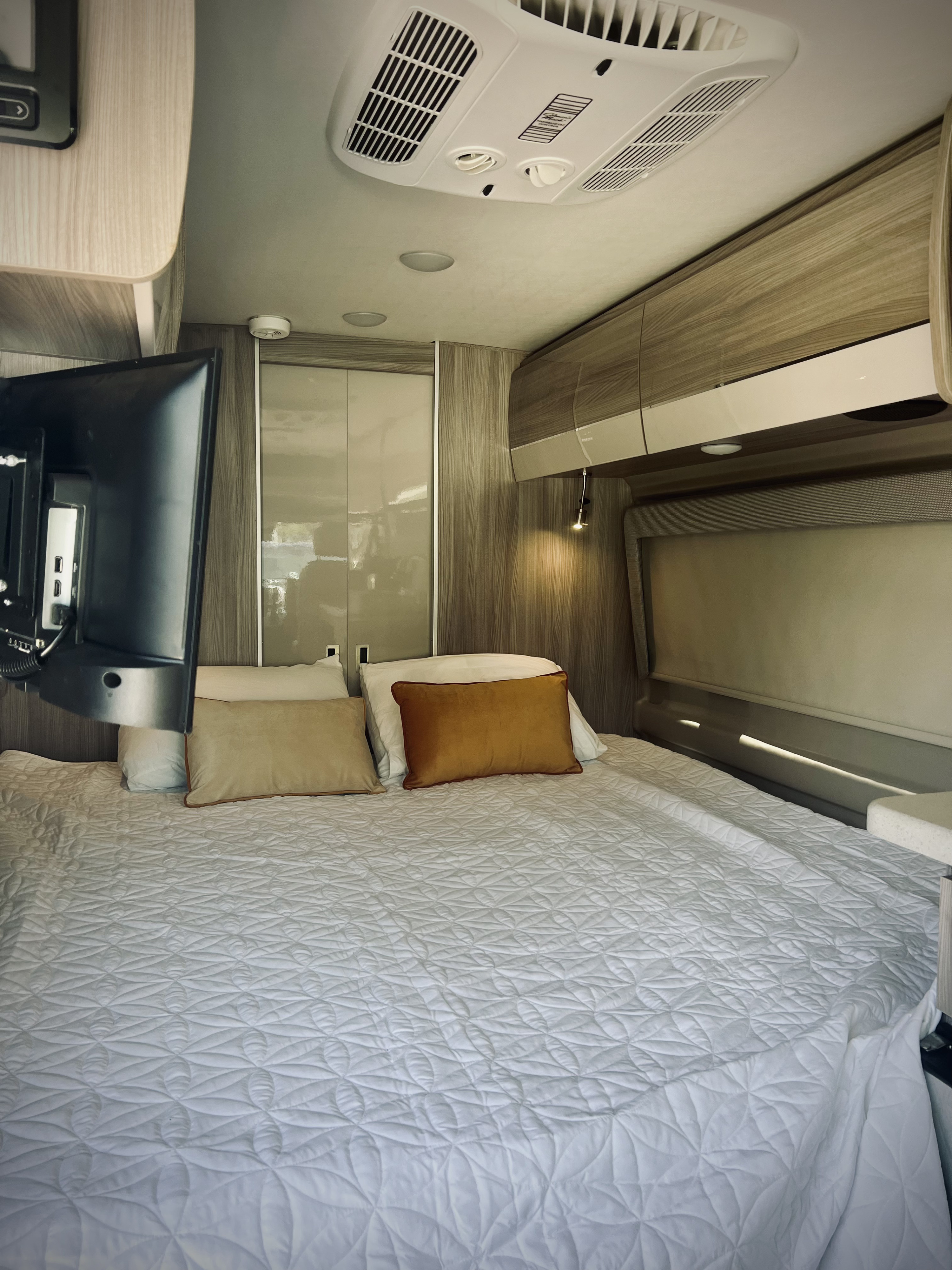 Modern RV rental bedroom featuring a large, inviting bed, TV, and overhead AC, ensuring comfortable travel stays.. Thor Sequence 2023