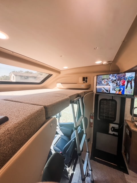 Interior of an **rv rental** showing an overhead bunk bed with ladder, the front cabin, and a TV playing a game.. Entegra Coach Qwest 24L 2024