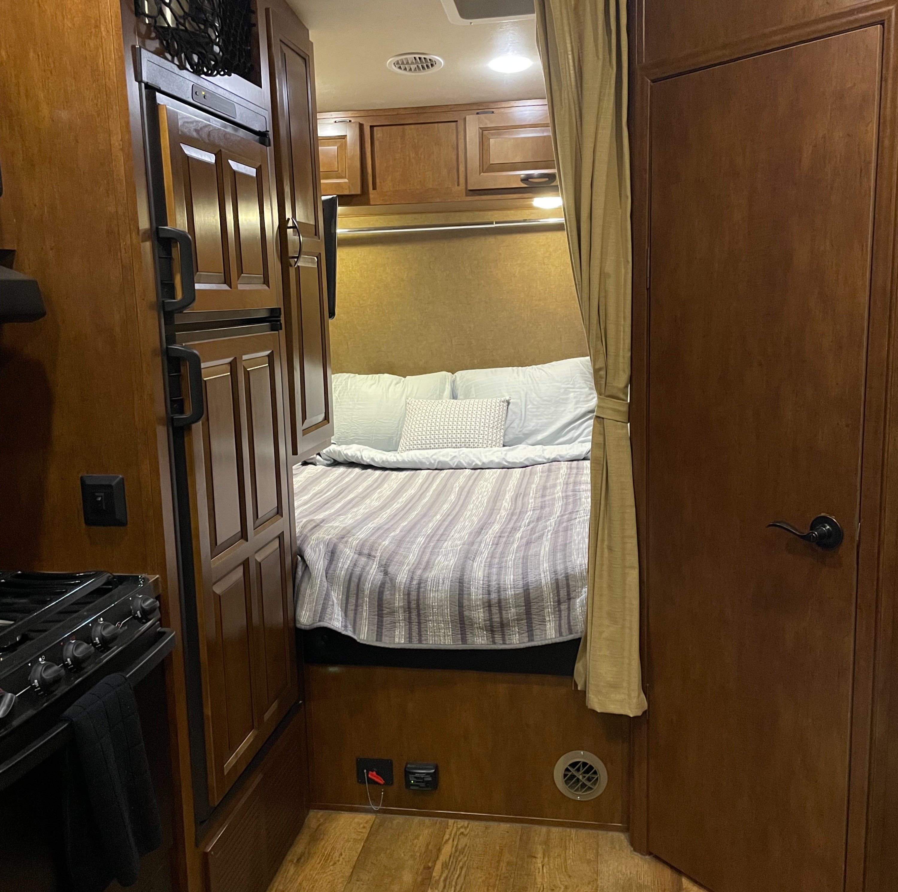 RV rental interior featuring a cozy bedroom area with a bed and adjacent kitchenette. Includes stove, fridge, and wooden cabinets.. Forest River Nitro Xlr 2015