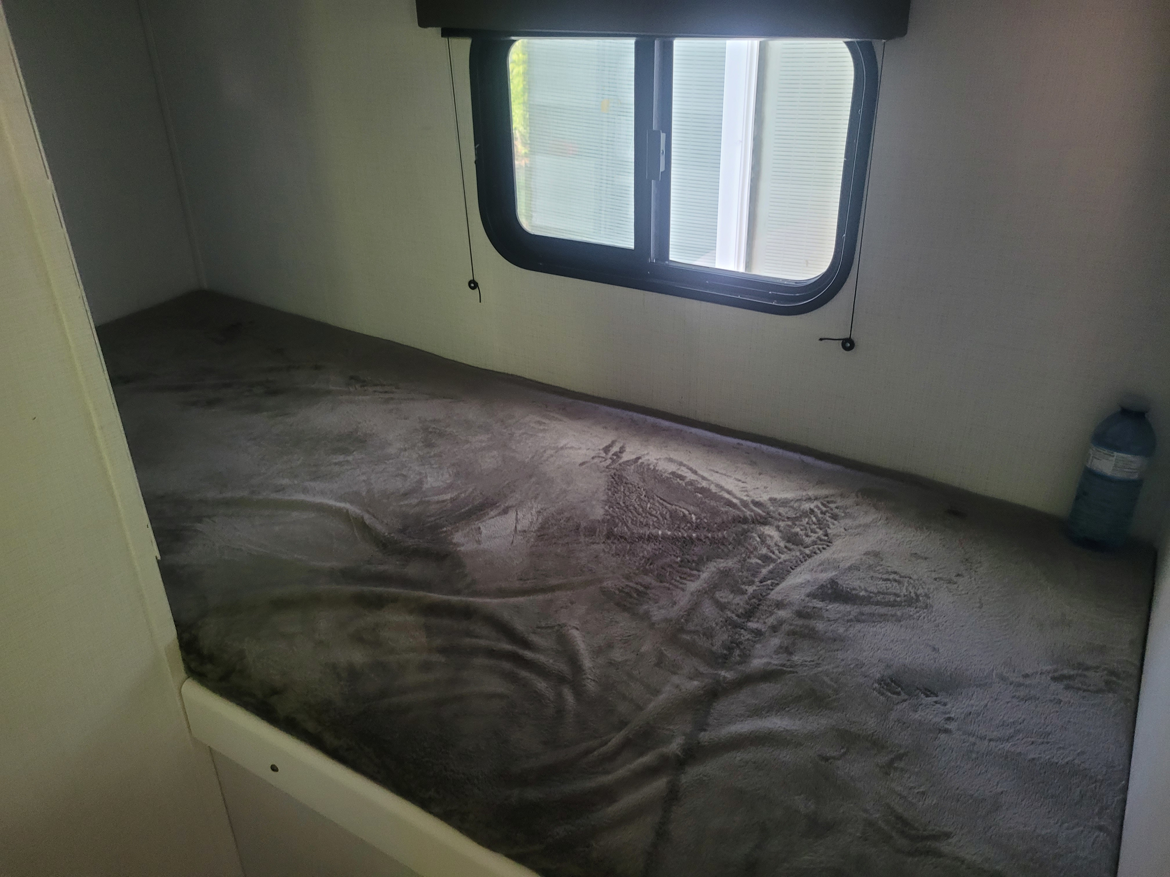 Inside an RV rental: a compact bunk bed with a soft grey blanket, window, and water bottle for travel.. Keystone RV Hideout 2022