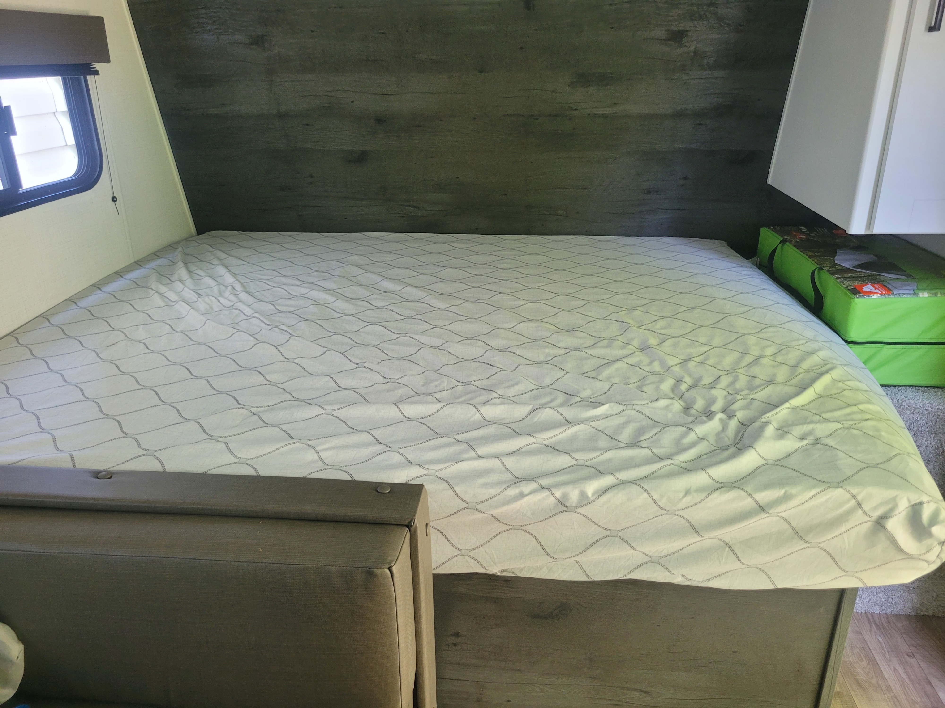 Spacious RV rental bed featuring a white patterned comforter, dark wood headboard, and window for your next adventure.. Keystone RV Hideout 2022