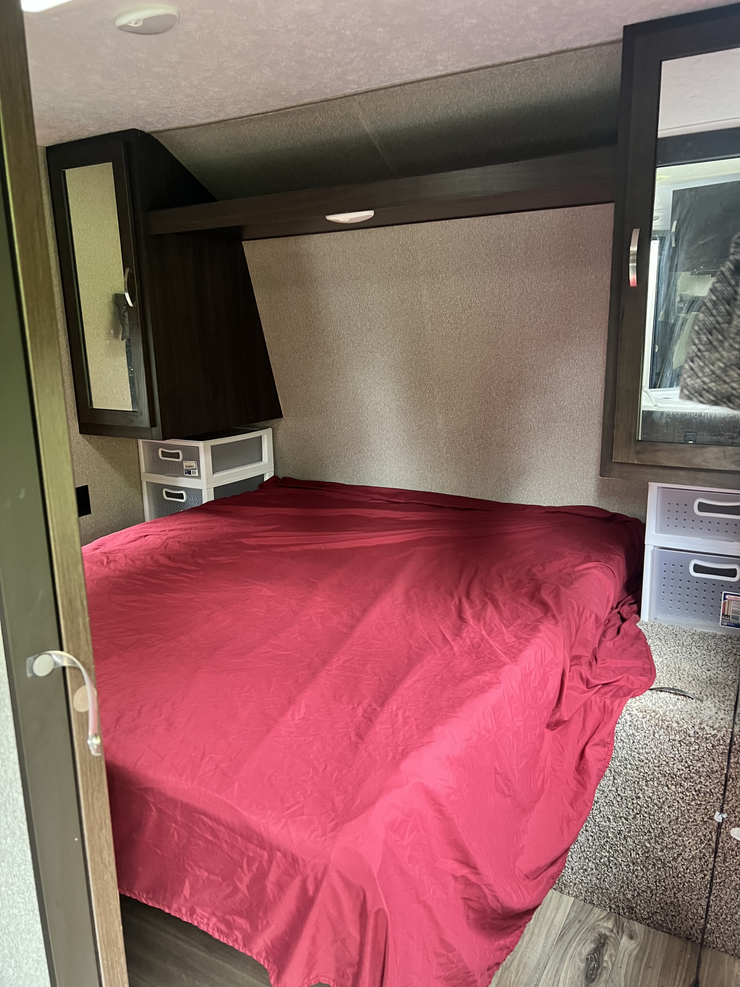 RV rental bedroom interior: a compact space with a red-covered bed, built-in cabinets, and side storage bins.. Keystone Springdale 2020