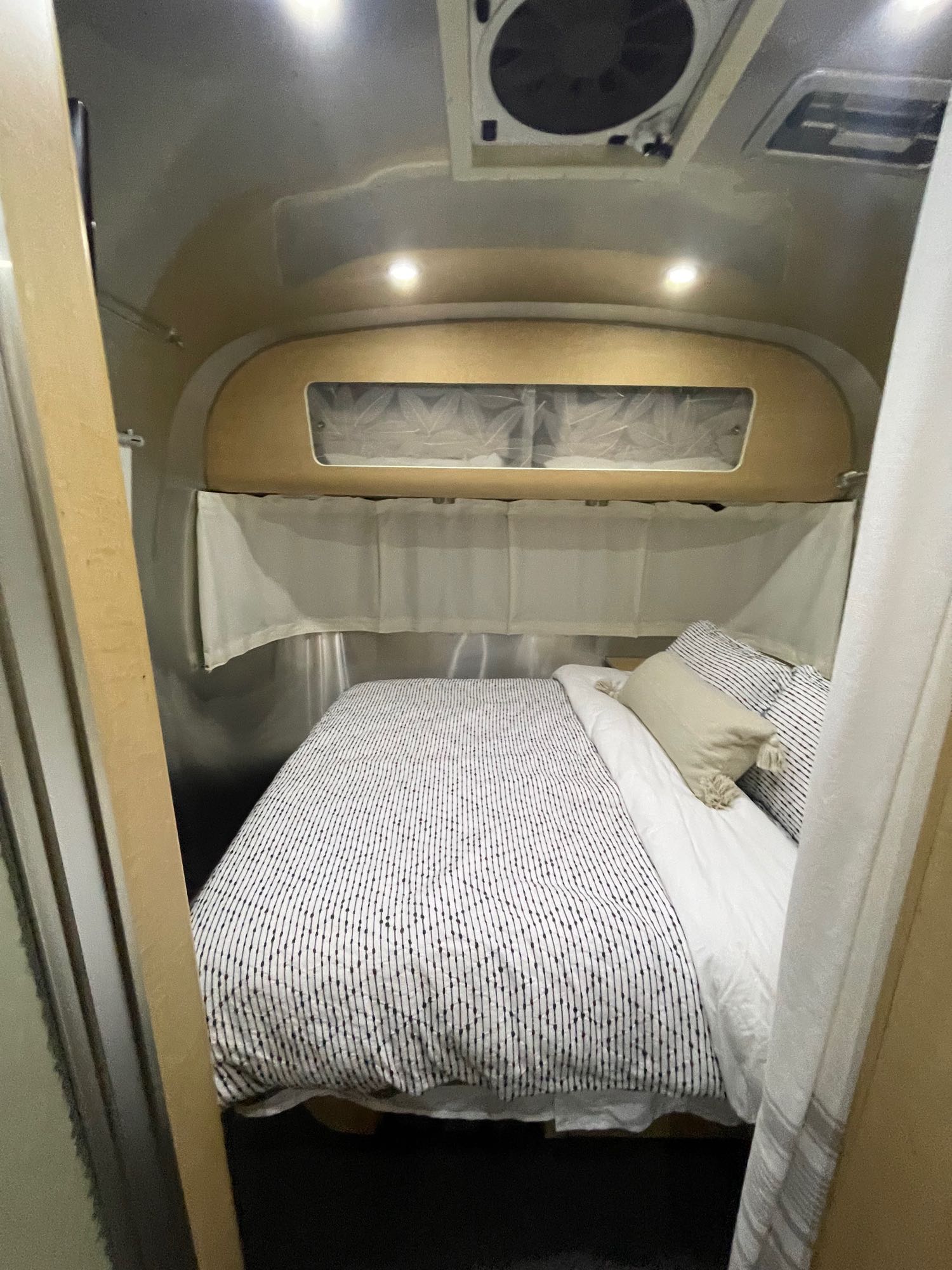 Modern RV rental bedroom. Features sleek metallic interior, cozy bed with striped bedding, and overhead storage/window.. Airstream Eddie Bauer 2012
