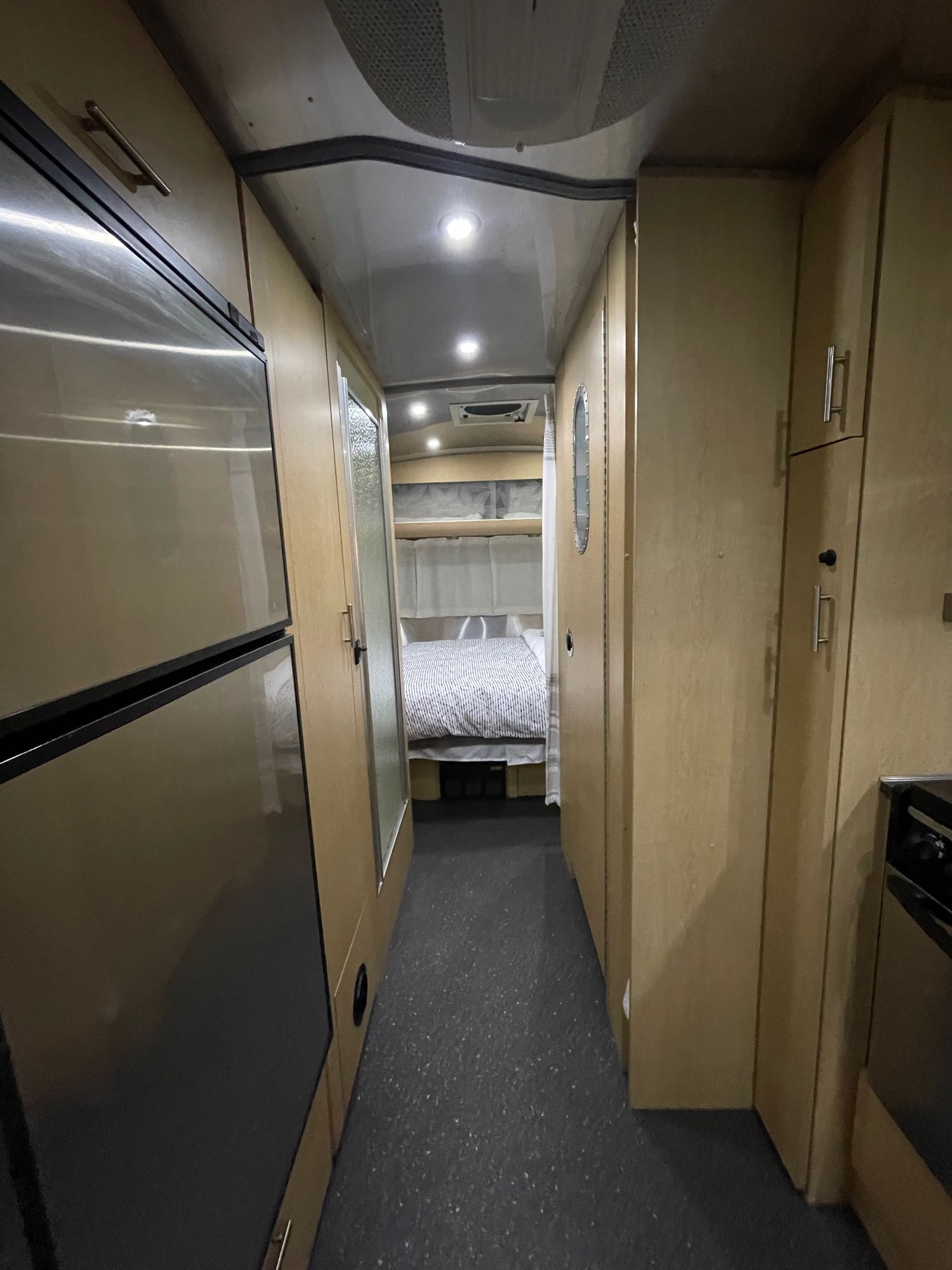 Inside this RV rental: a compact interior hallway leading to a bedroom, with kitchen appliances on the left and cabinets on the right.. Airstream Eddie Bauer 2012