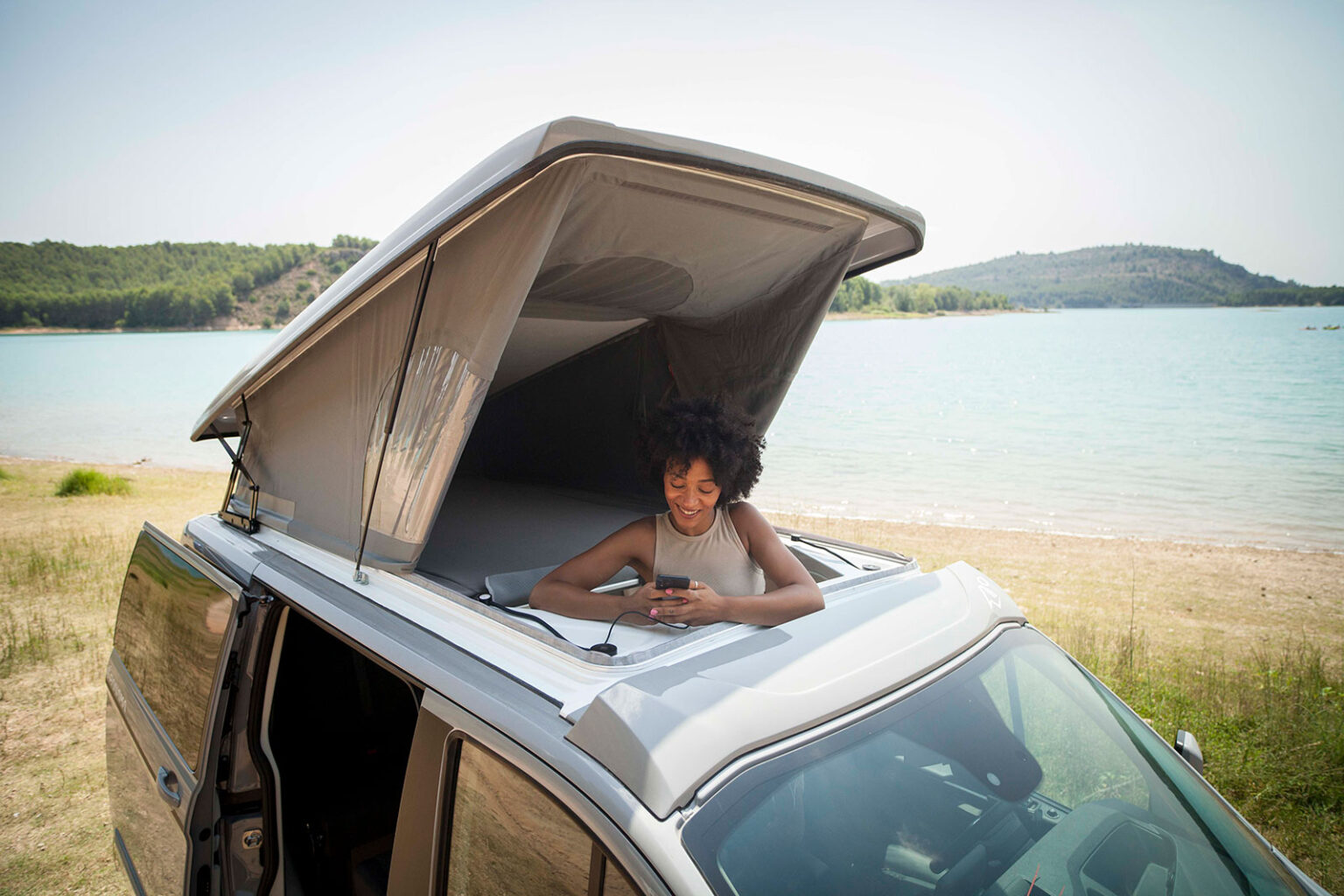 Connected tranquility: Woman smiles on phone in a pop-top RV rental by a lake. Ideal for scenic getaways.. Panama P10+ 2023