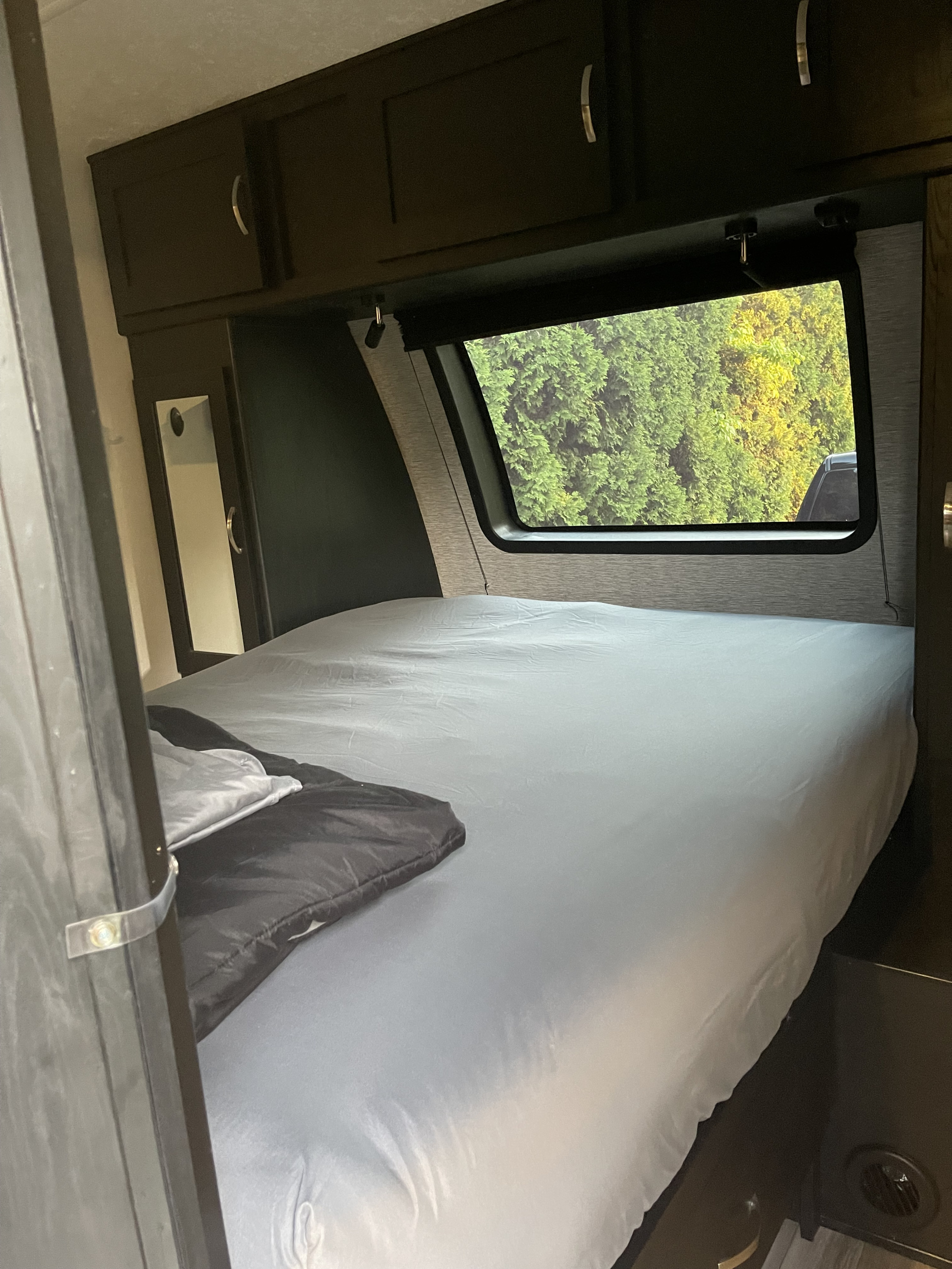Cozy RV rental bedroom featuring a neatly made bed, overhead cabinets, and a window with a view of lush green trees.. Coachmen 292BHDS FREEDOM EXPRESS LIBERTY EDITION 2022