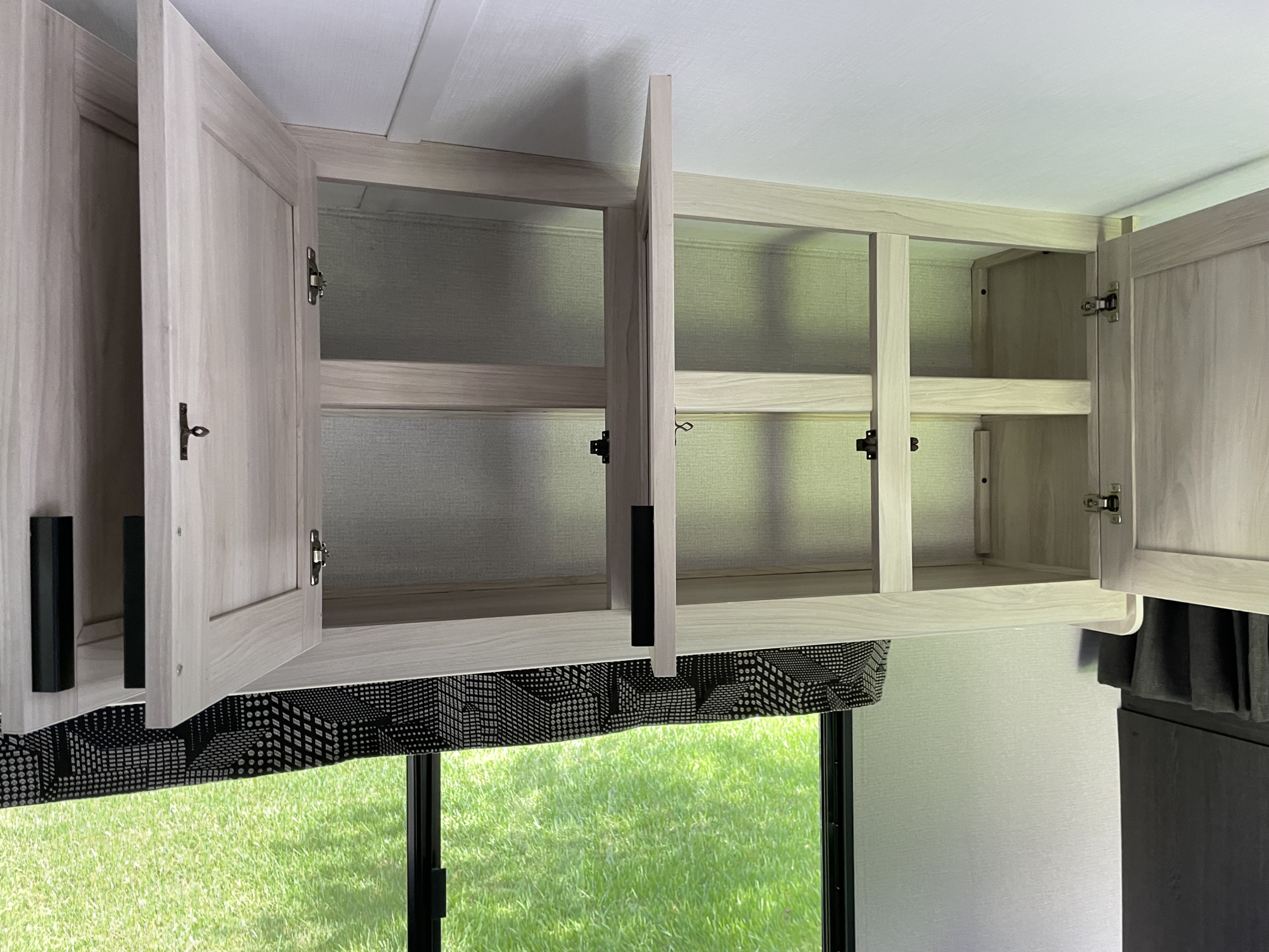 RV rental interior featuring open light wood overhead cabinets with shelves, offering a view of green grass outside.. Forest River Sunseeker LE 2023