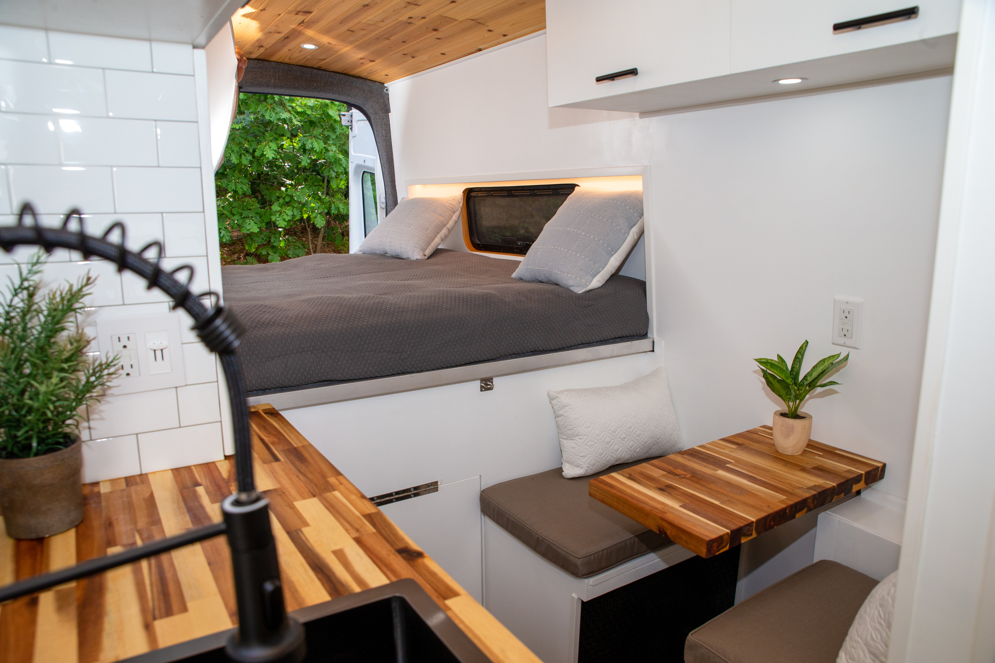 Modern RV rental interior with a raised bed, full kitchen, and dinette. Features a sleek design with wood accents and white walls.. Ford Transit 2018