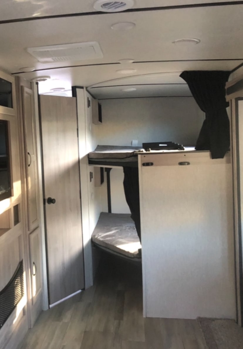 Interior view of an RV rental, featuring stacked bunk beds and a bathroom door, perfect for family camping adventures.. Coachmen 2963BH 2021