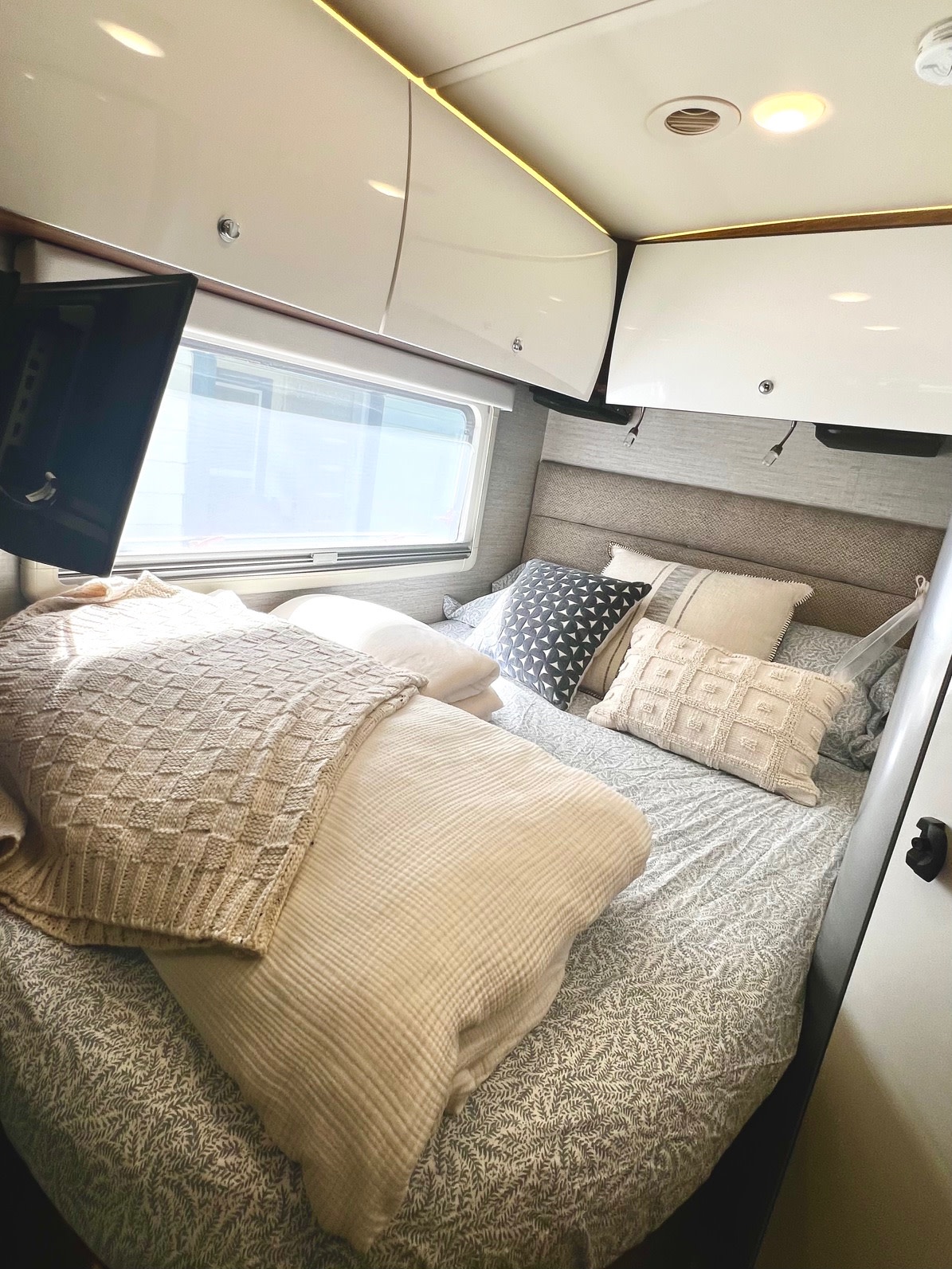 Cozy RV rental bedroom featuring a comfortable bed with multiple pillows and blankets, plus compact overhead storage and a TV.. Winnebago View 2022