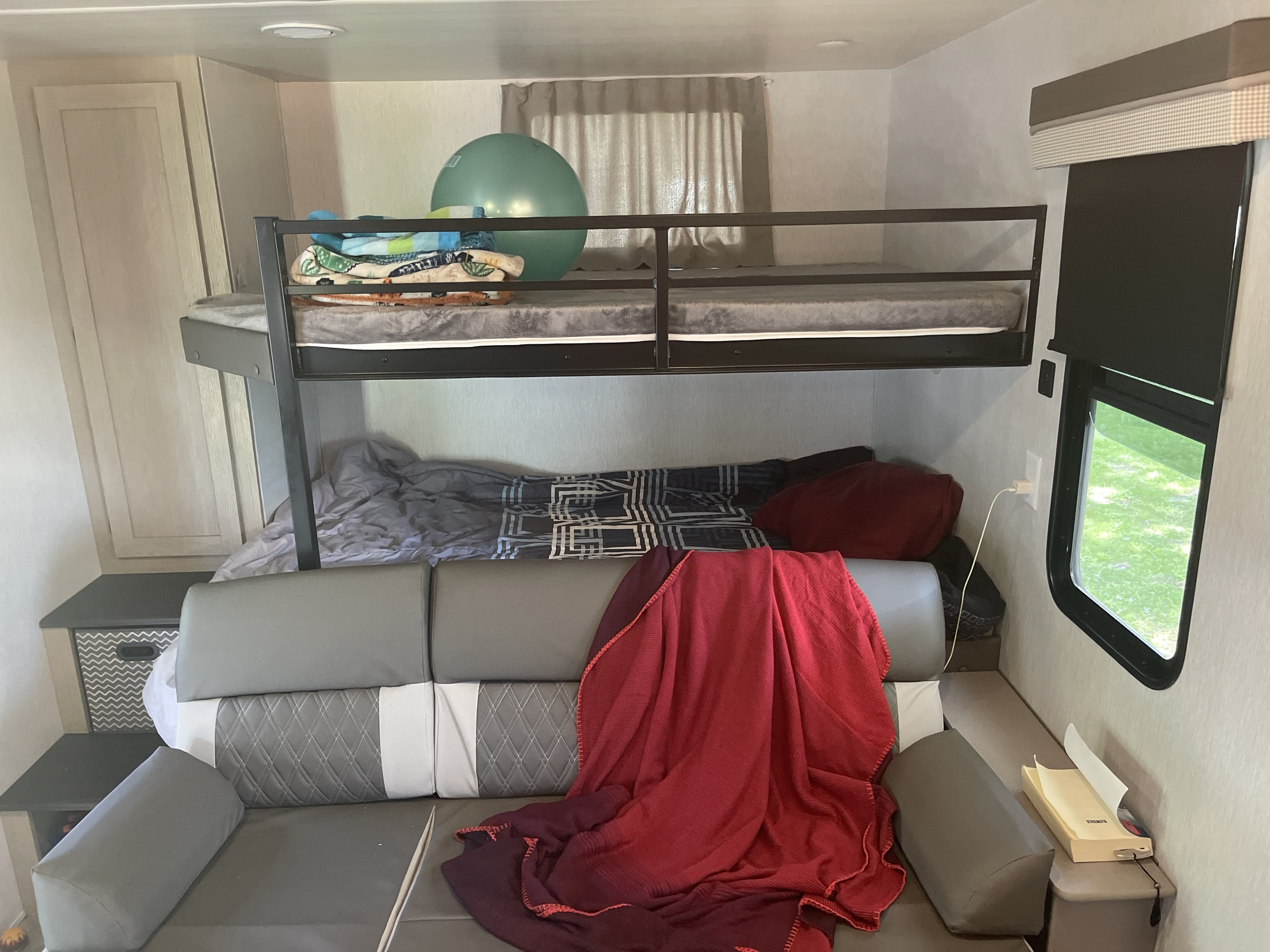 RV rental interior: bunk beds above a convertible couch, with storage and a window.. Forest River Wildwood 2023
