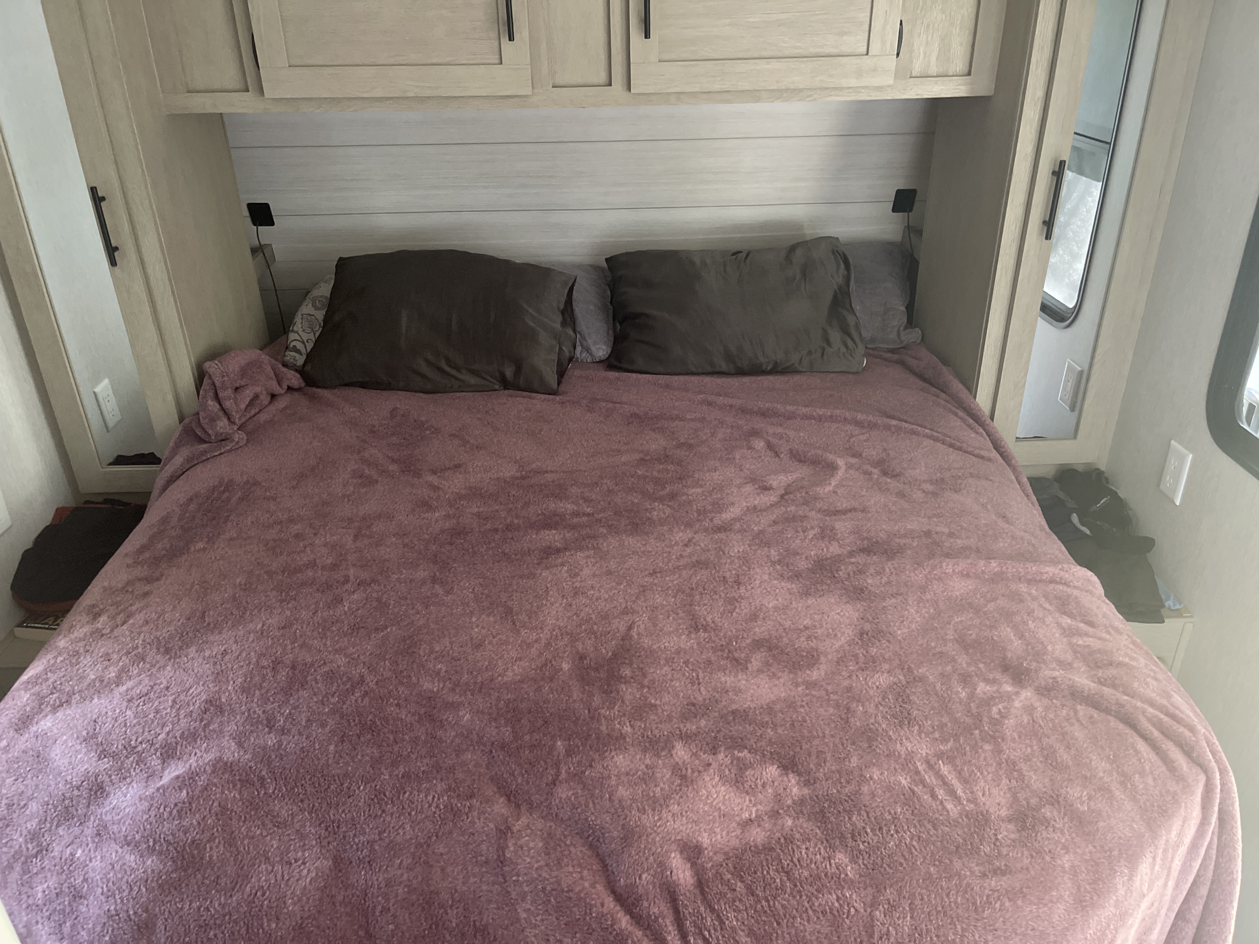 Cozy RV rental bedroom with a soft purple blanket, pillows, and overhead storage, designed for comfortable travel.. Forest River Wildwood 2023