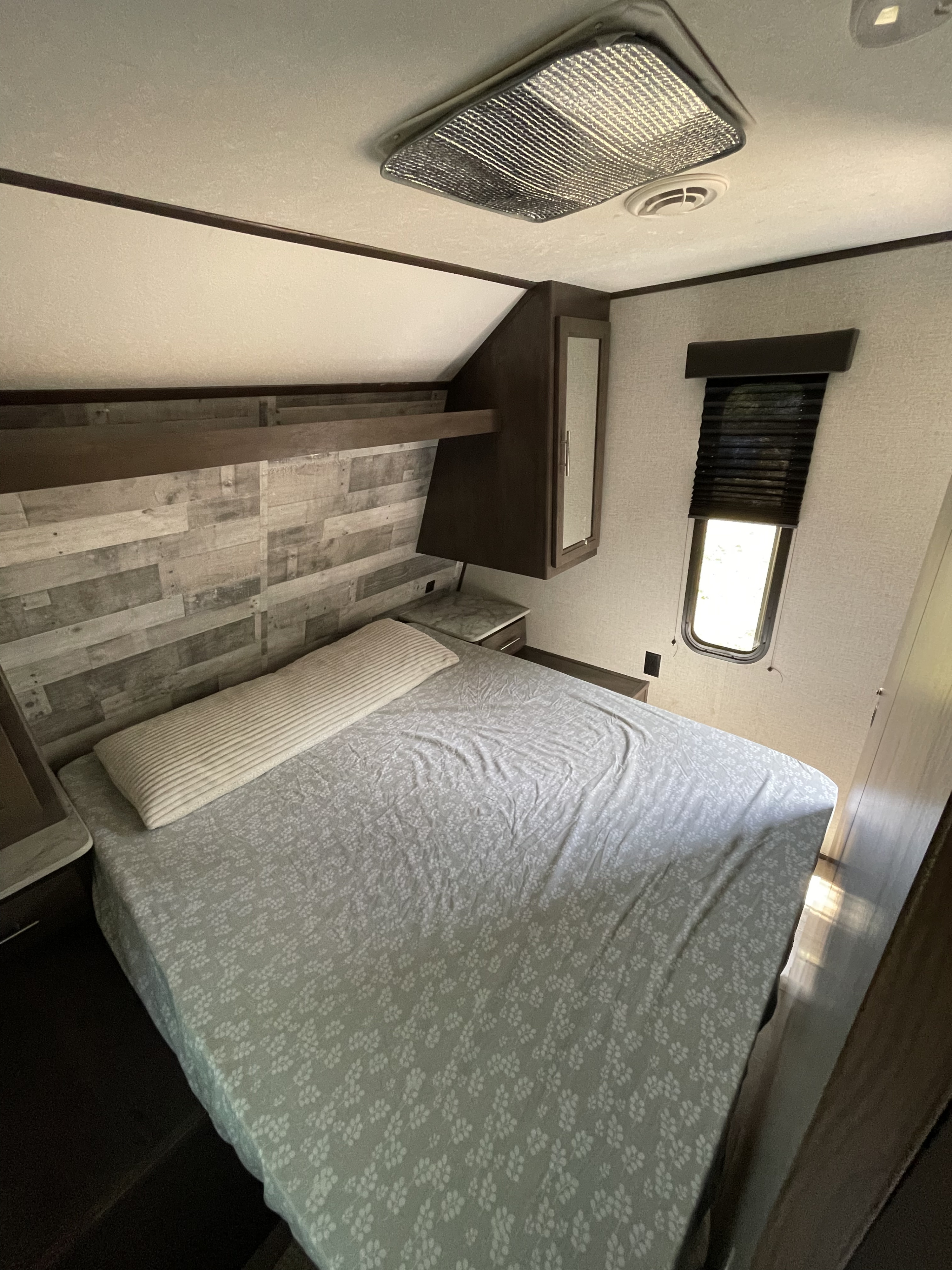 Cozy RV rental bedroom featuring a patterned bed, wood accent wall, and compact built-in storage. Perfect for road trips.. Dutchmen Coleman Lantern 2021