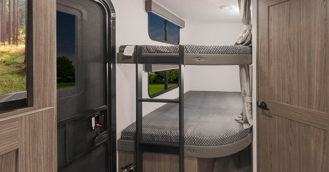 Cozy RV rental interior featuring two bunk beds with a ladder, a wooden door, and windows showing nature outside. Perfect for trips.. Alliance Delta 251BH 2024