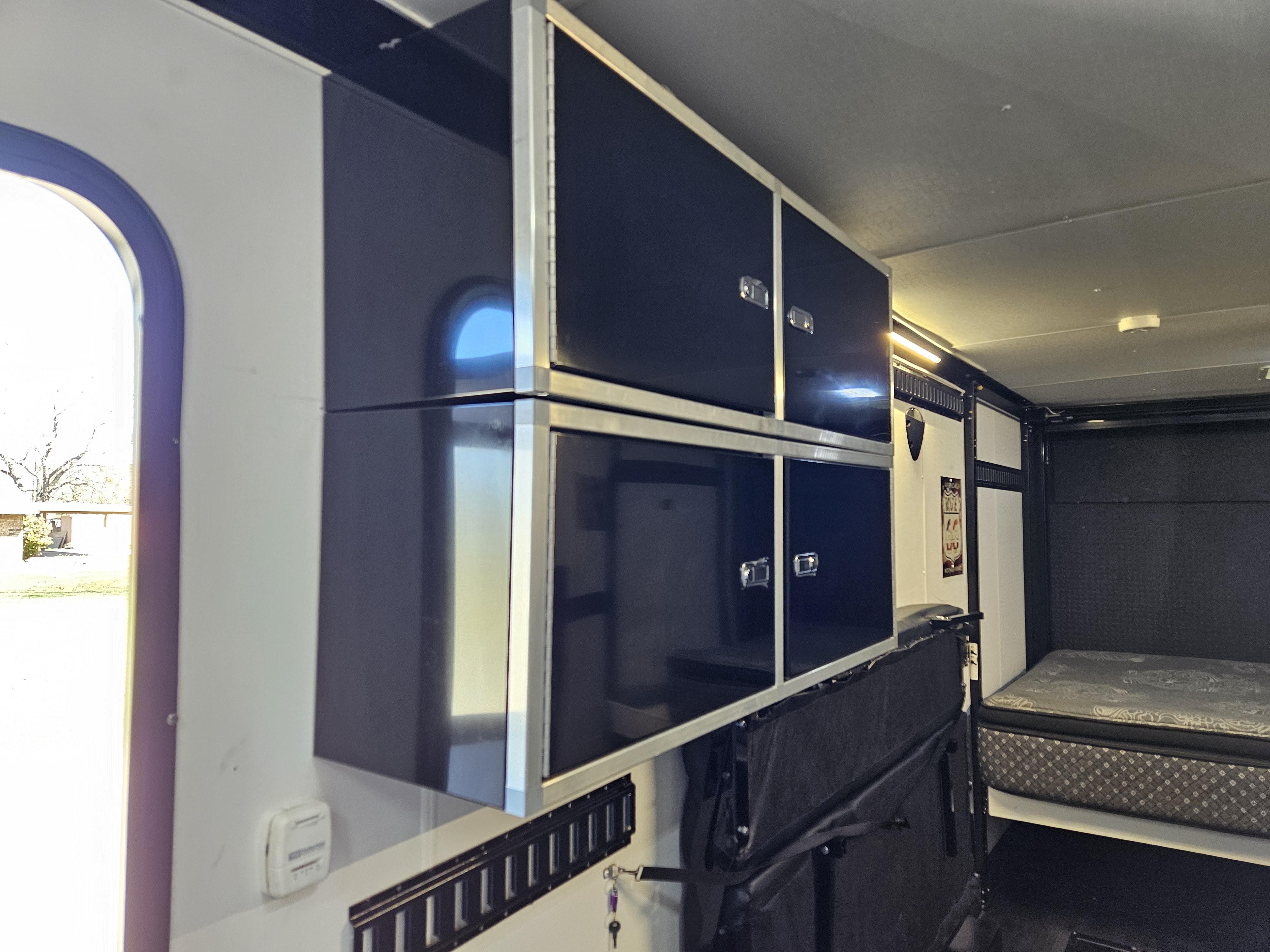 RV rental interior featuring sleek black overhead storage cabinets, a comfortable bed, and a bright window.. Stealth Nomad 2021