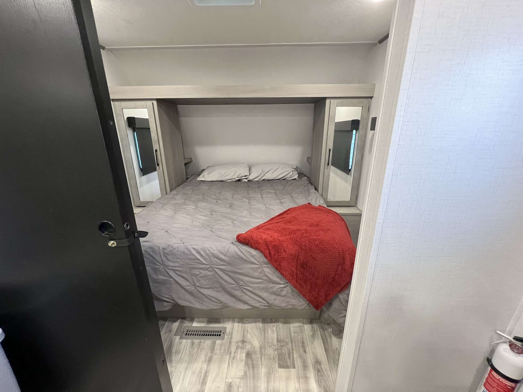 Comfortable RV rental bedroom with a grey bed, red blanket, and integrated storage, offering a cozy space for travel.. Dutchmen Kodiak SE 2024