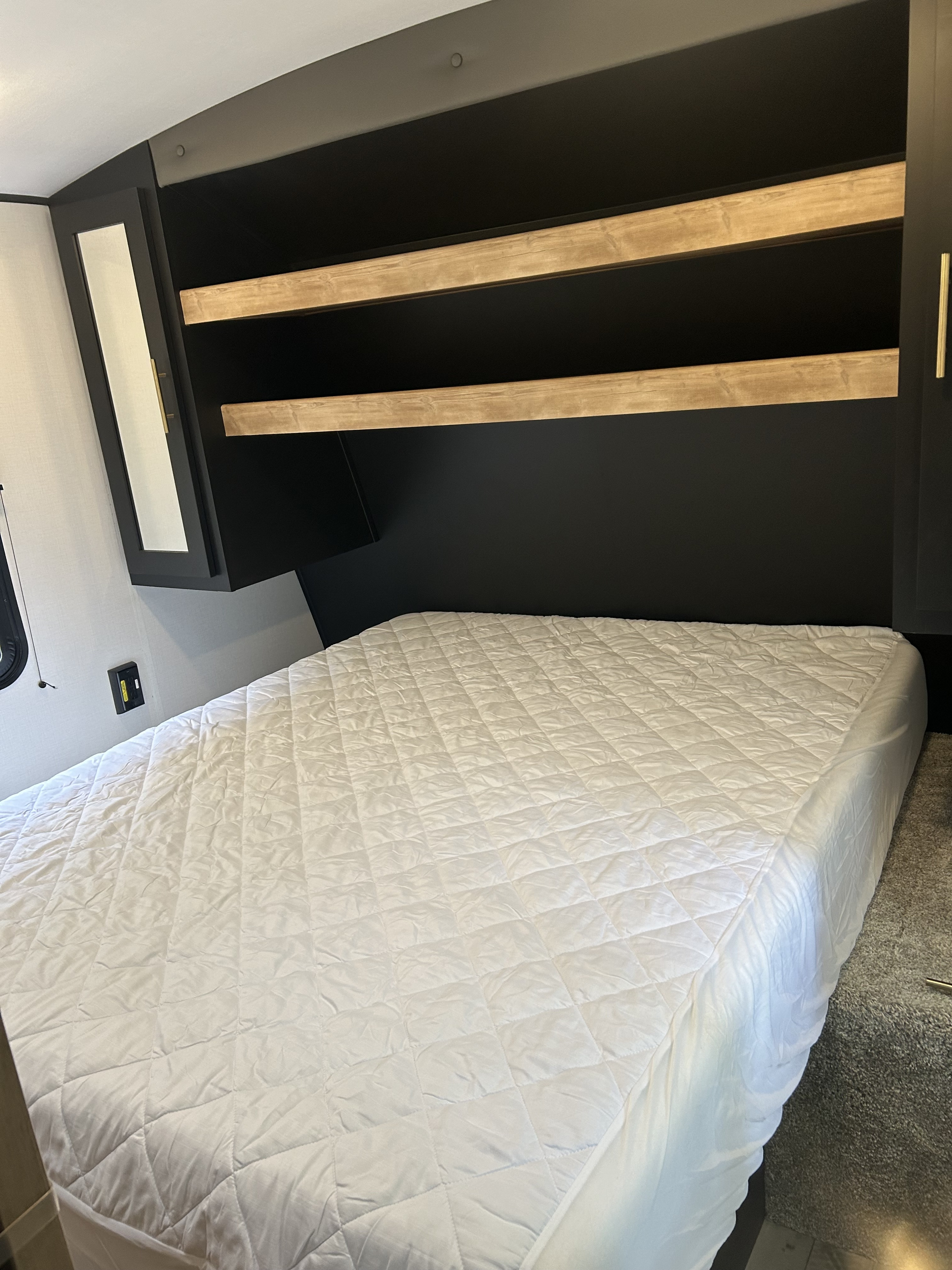 This RV rental bedroom offers a comfortable, quilted bed with dark headboard, practical shelves, and storage.. Keystone Springdale 2023